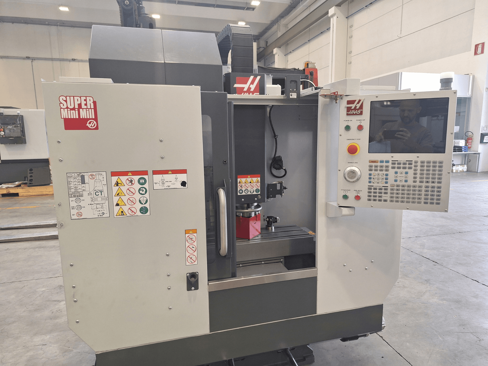 HAAS Super Mini Mill front view showing control panel, safety labels, and machining area with a workpiece setup.