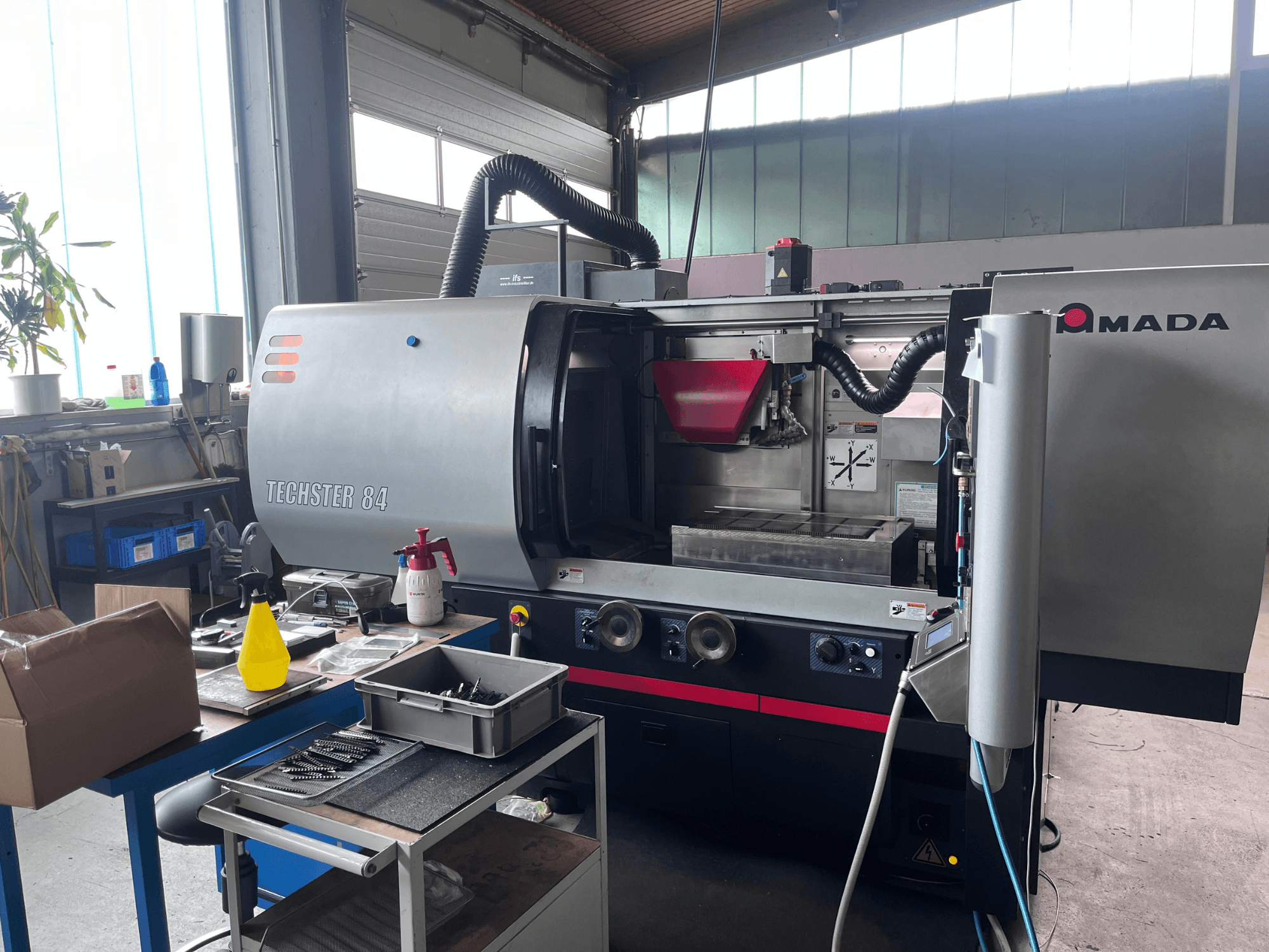 AMADA Techster 84 surface grinding machine in a workshop, showcasing a front view with operational controls and red hopper.