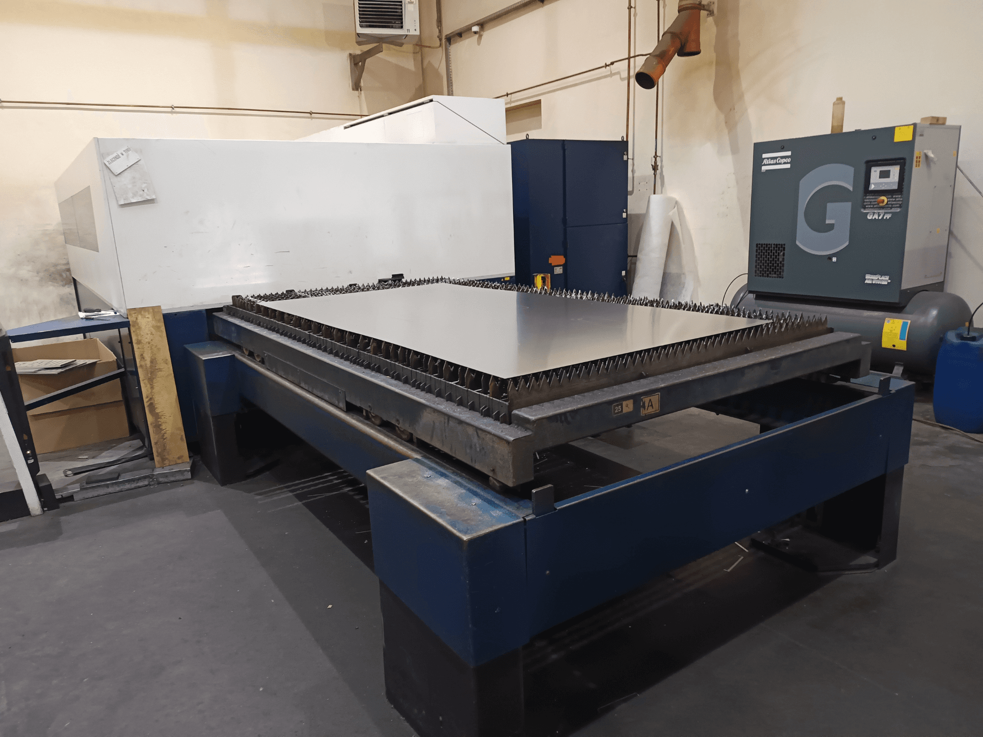 Industrial cutting machine with metal table, front view. Features sharp edges, air compressor on the right, and steel frame.