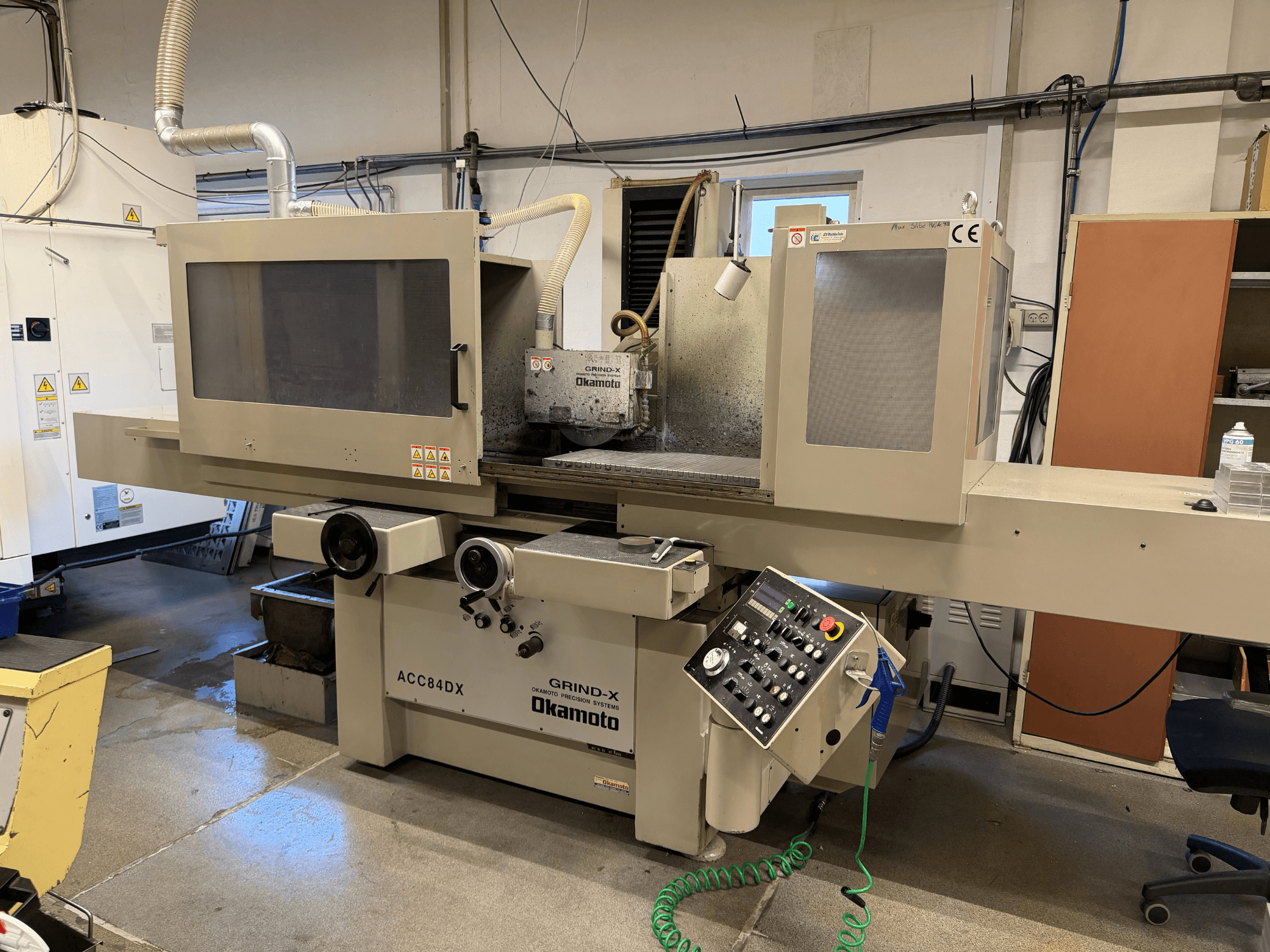 Front view of OKAMOTO ACC 84DX surface grinding machine featuring control panel and coolant system.
