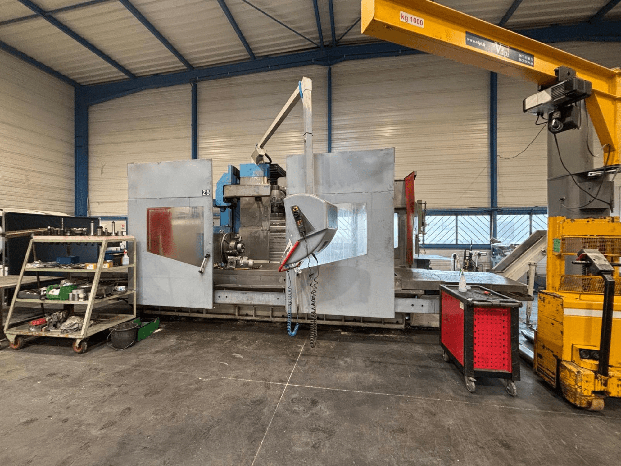 CNC milling machine from side view in a workshop; visible tools and storage shelves. Brand and model not specified.