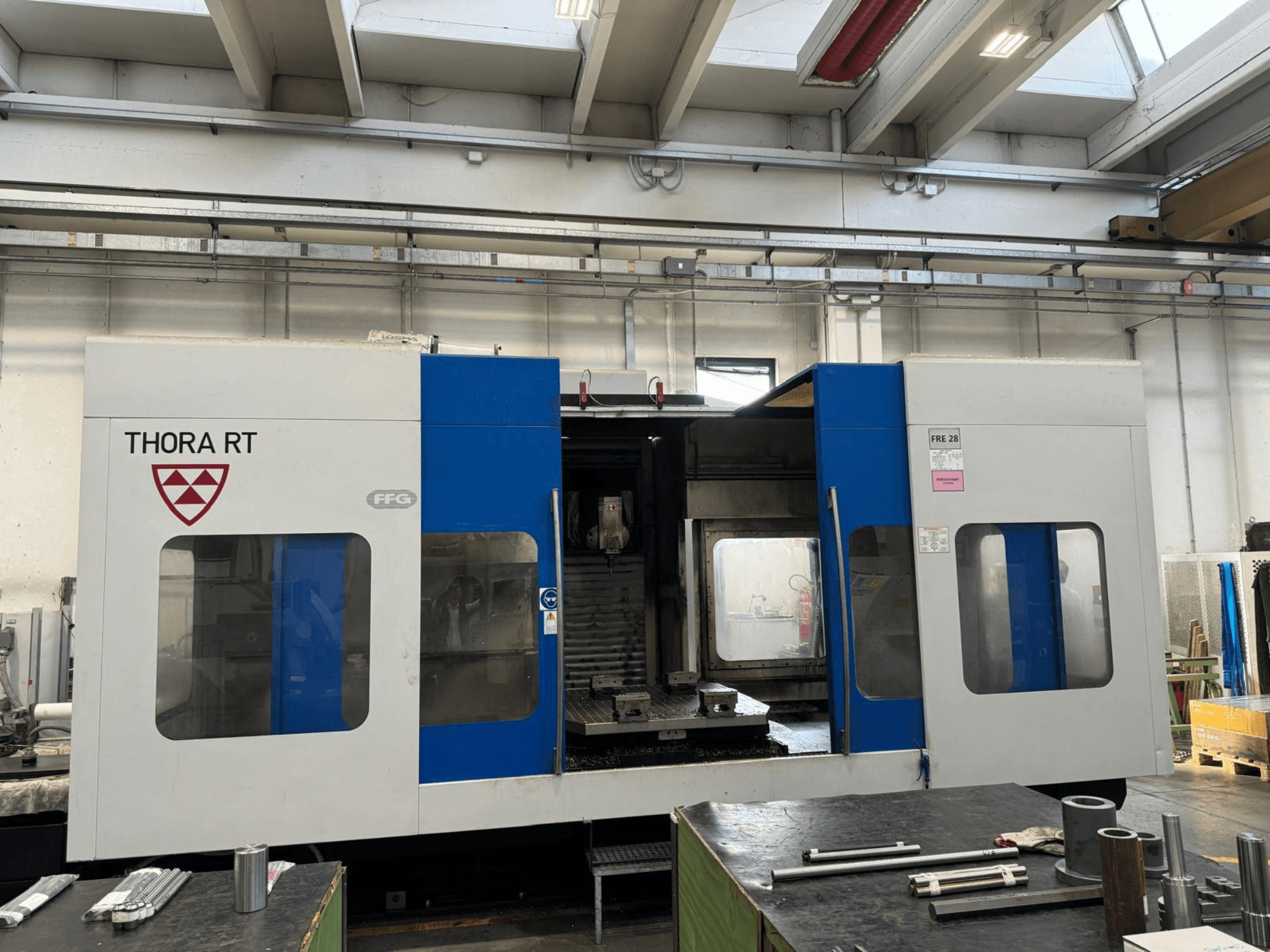 THORA RT CNC machine viewed from the front, featuring a blue and white exterior, transparent windows, and mounted tools.