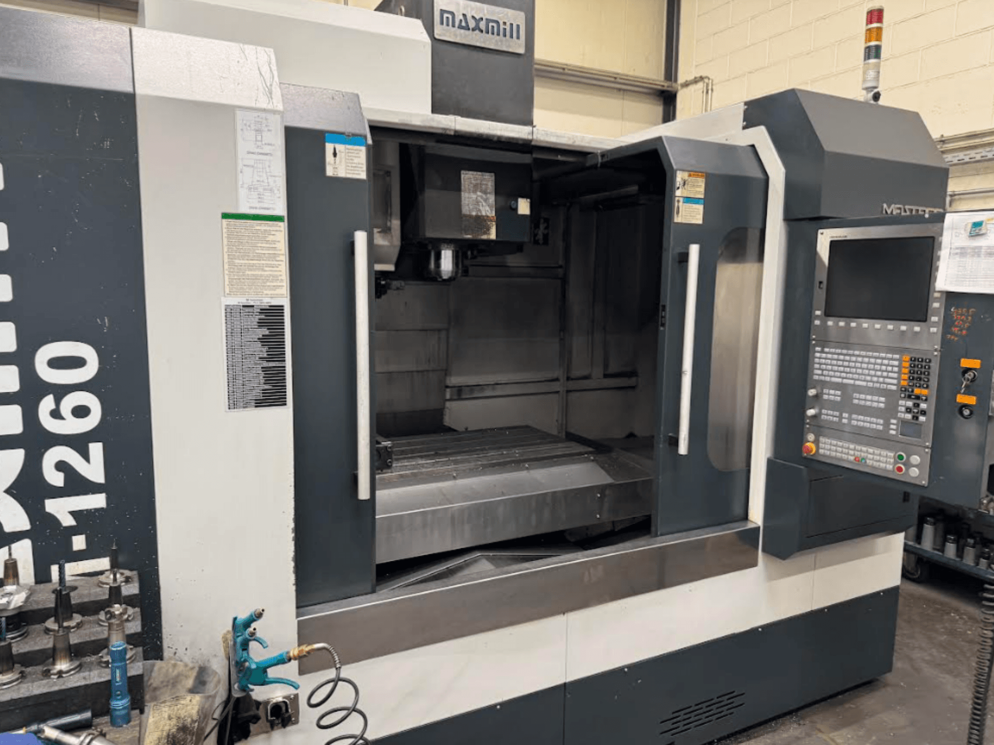 Maxmill CNC milling machine, model M-1260, front view showing empty workspace with control panel and operational instructions.