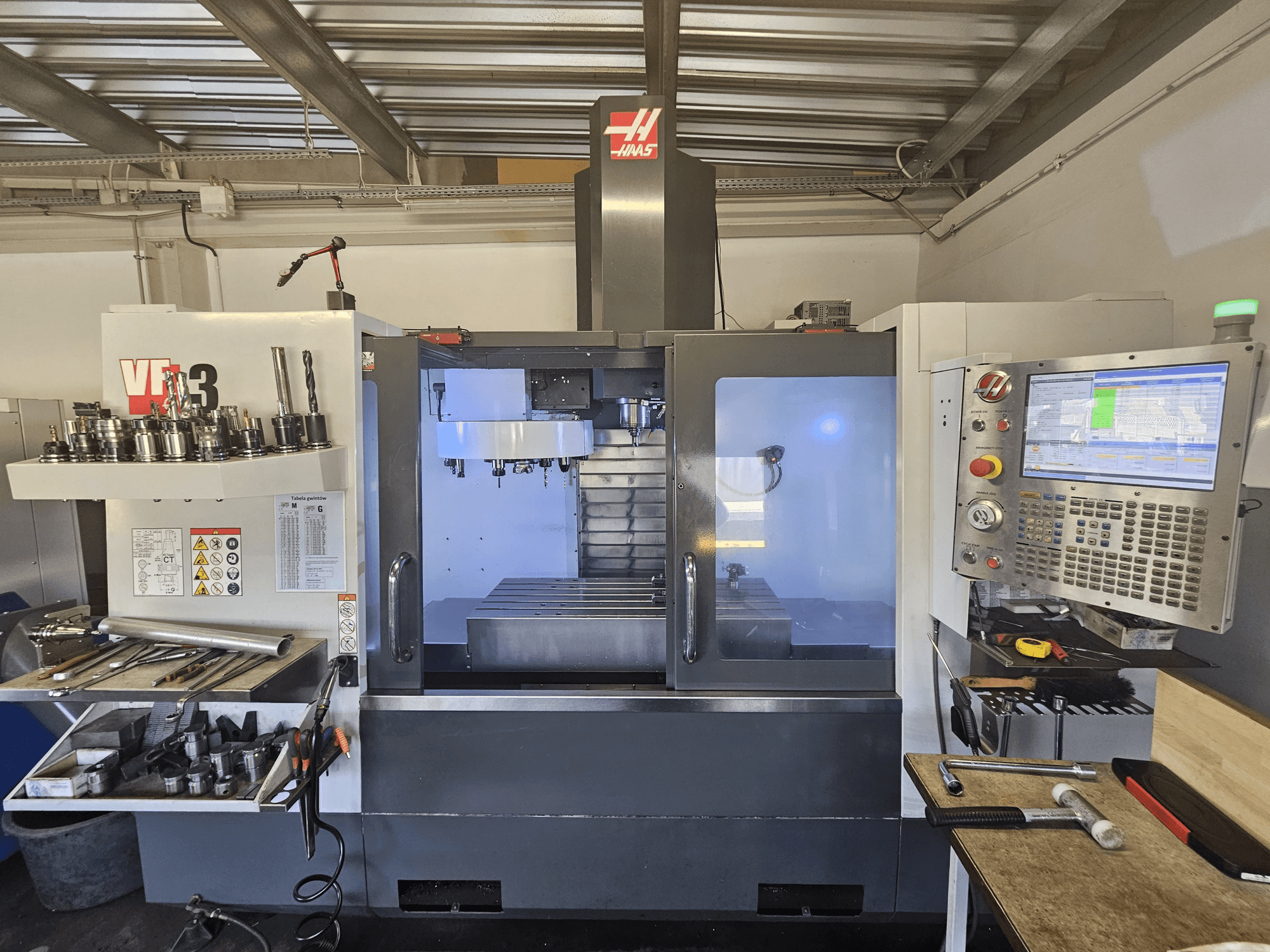 Haas VF-3 CNC machine in a workshop, front view displaying tools, controls, and milling area with illuminated interior.