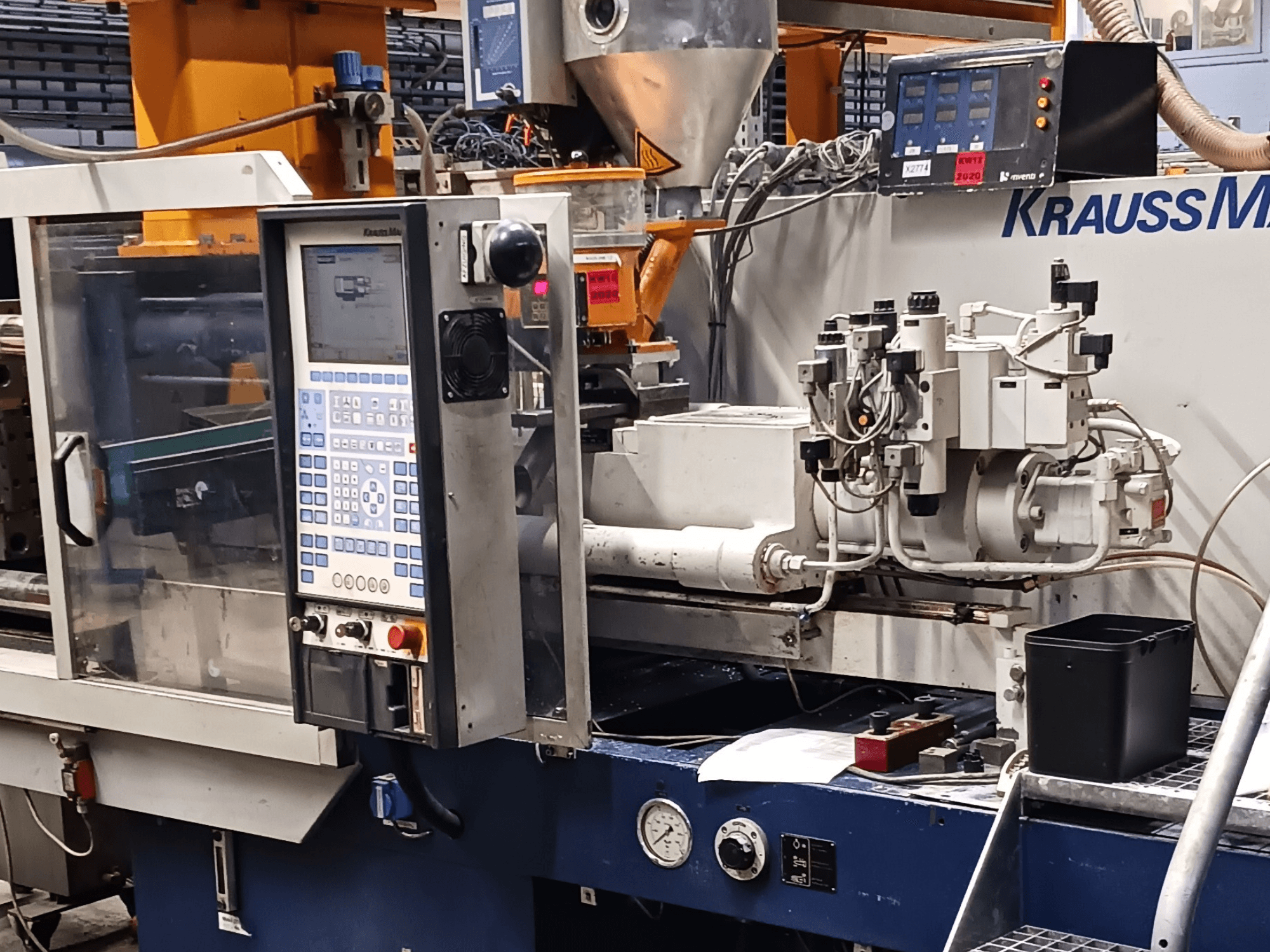 KraussMaffei injection molding machine with control panel, hydraulic units, and tools in foreground, front view.