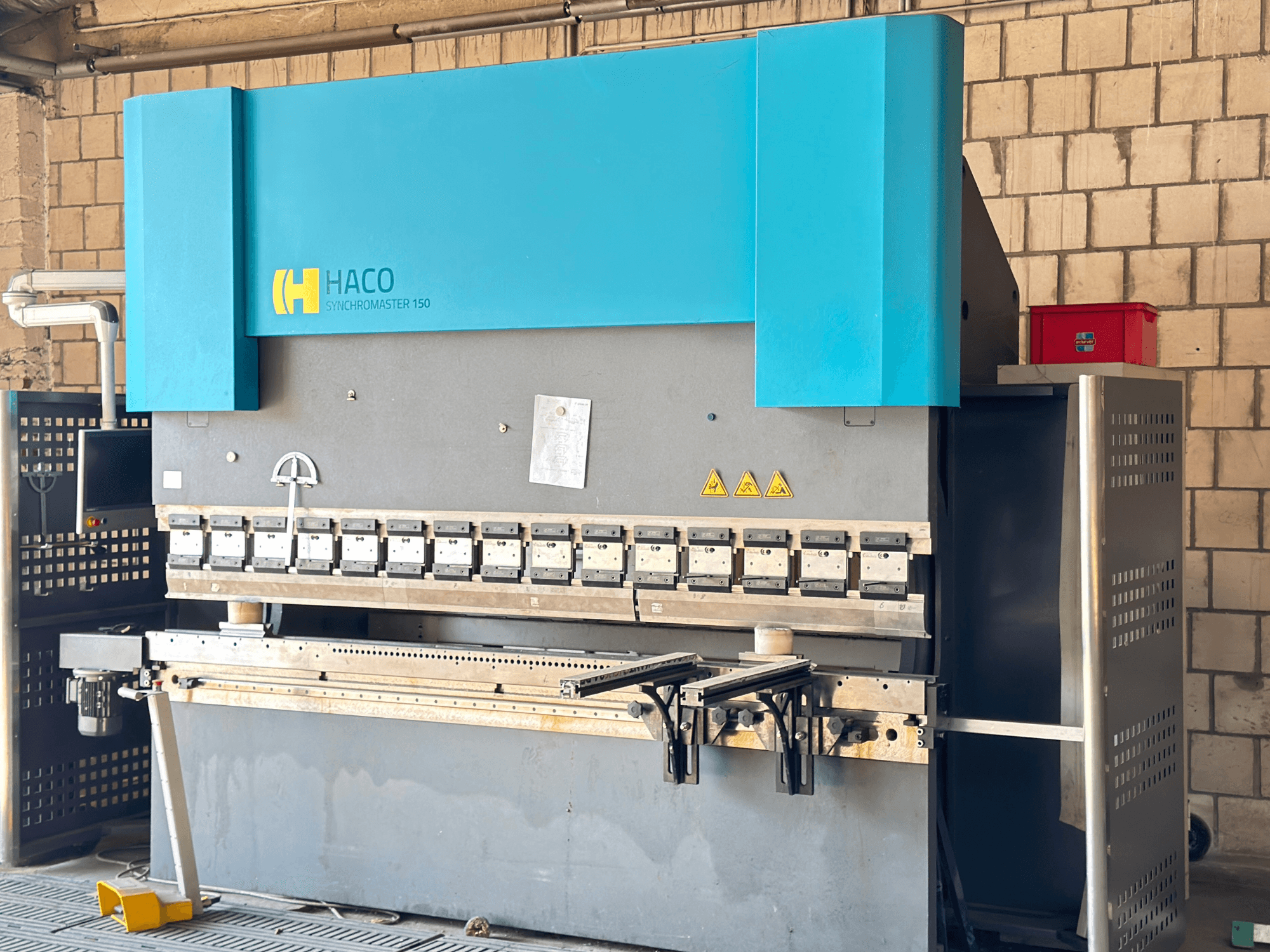 Press brake HACO SRM30150, front view; includes control panel and clamping dies, with safety warning labels visible.