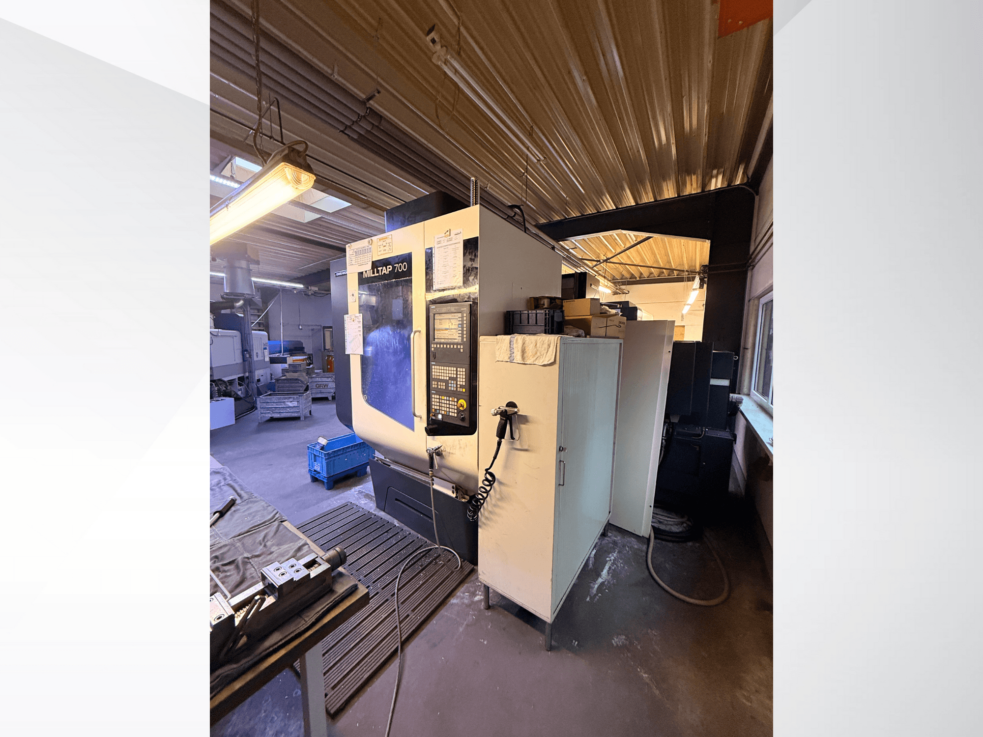 Milltap 700 CNC machine in workshop; front view shows control panel, tool racks, and storage areas with lighting above.