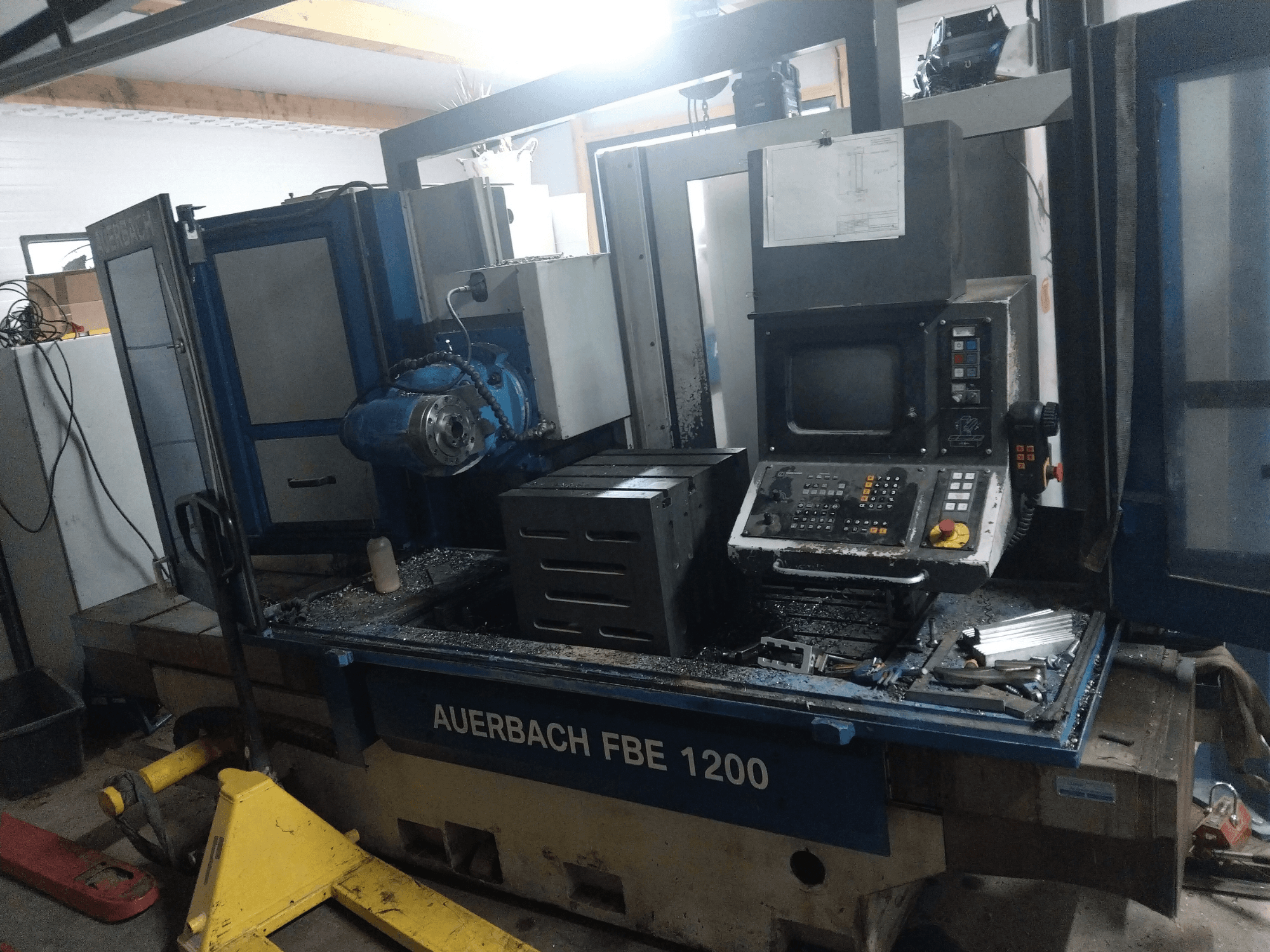 Auerbach FBE 1200 metal drilling machine, front view, showing control panel, motor, and metal shavings on work surface.