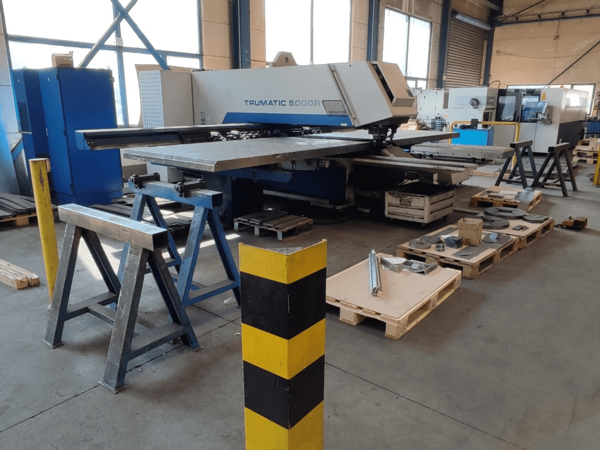 TRUMPF Trumatic 5000 R CNC punching machine in a workshop, side view with tools and materials on pallets nearby.