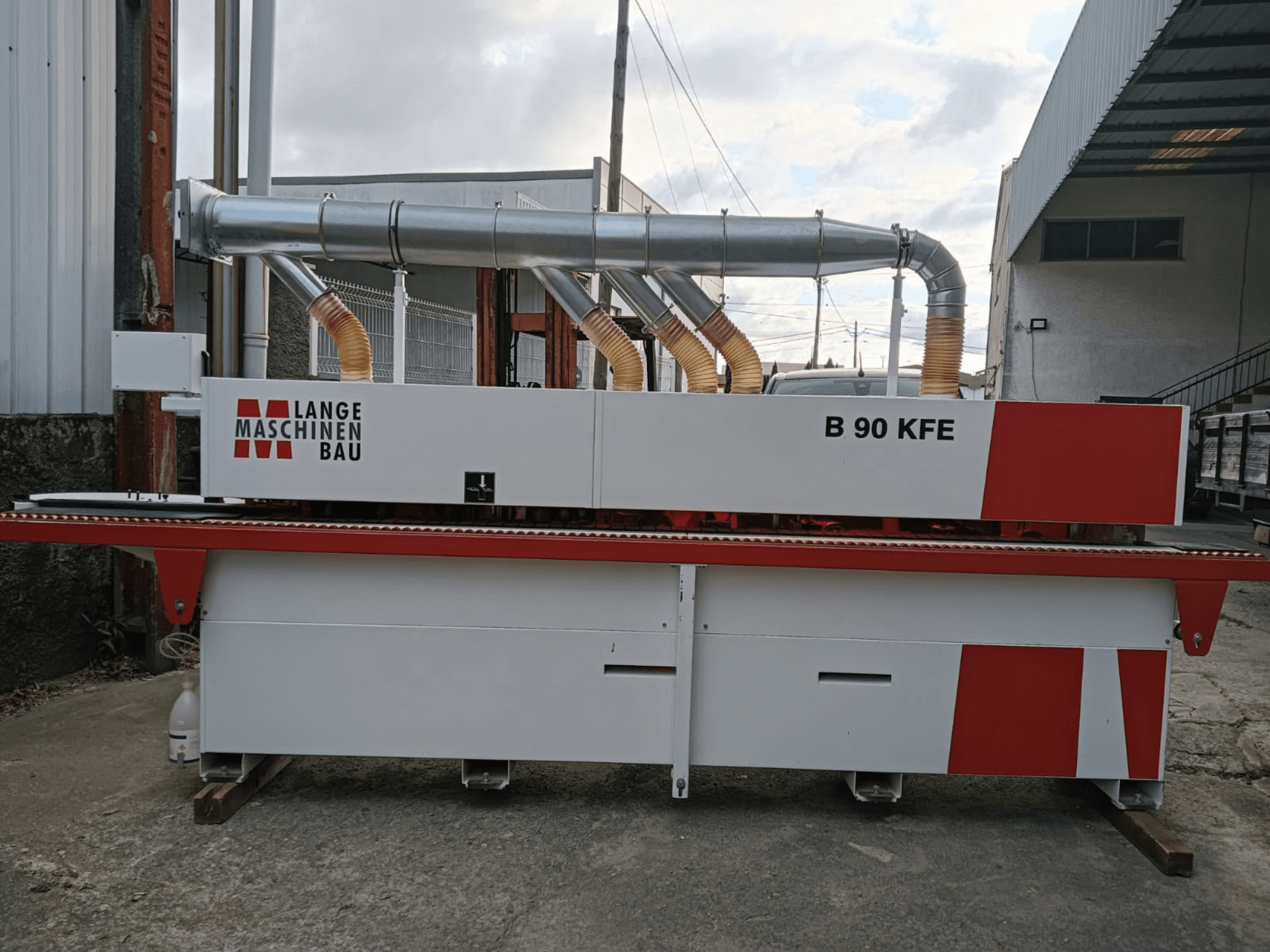 LANGE Maschinenbau B 90 KFE edgebander in side view with dual exhaust pipes and red accents, set in an industrial workspace.
