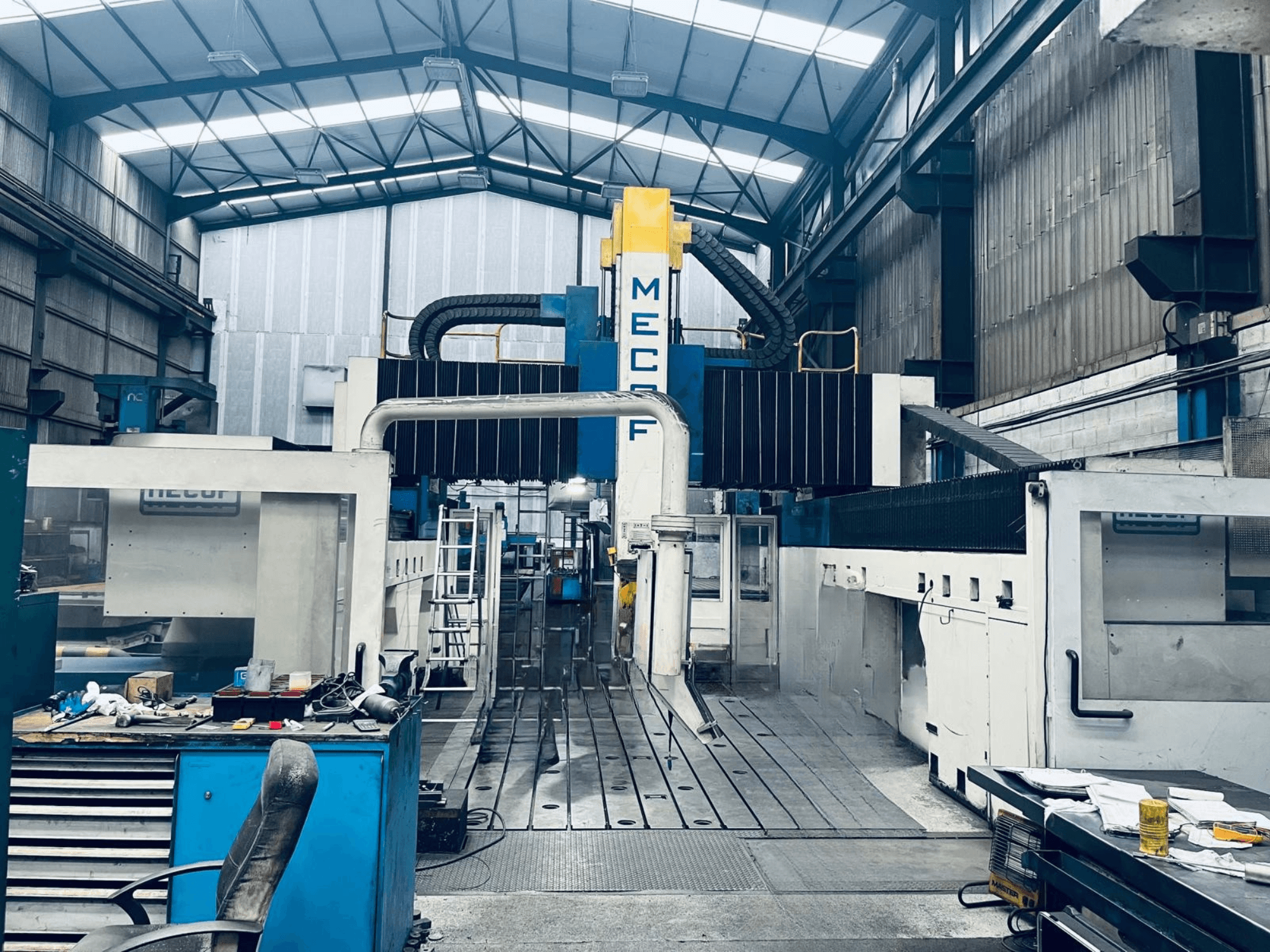 Gantry milling machine MECOF DYNAMILL 3000L in workshop, front view, showcasing blue and white structure, tools, and workspace.