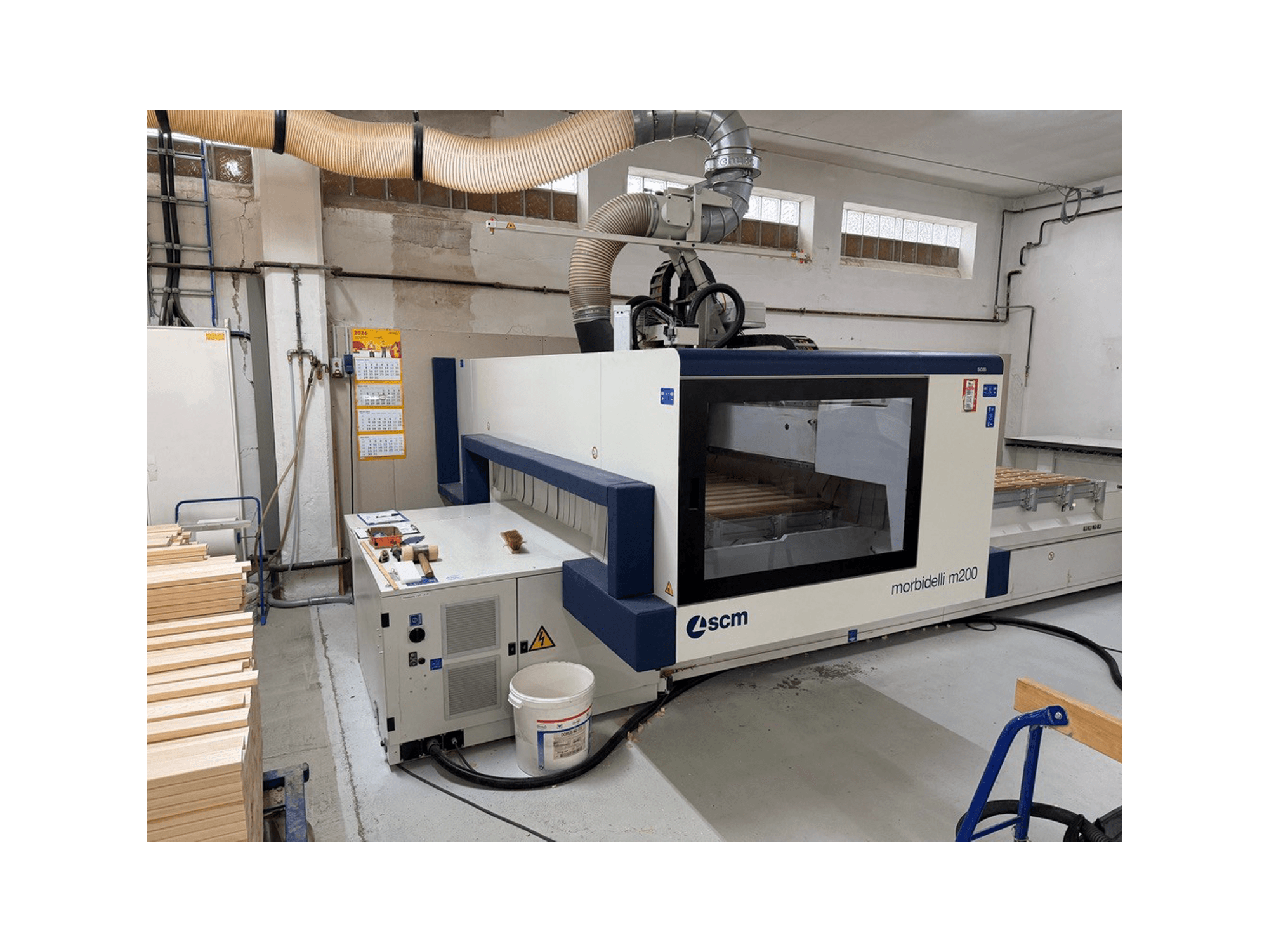 SCM Morbidelli M200F CNC processing center in a workshop, side view with wood pieces on the table and ventilation system above.