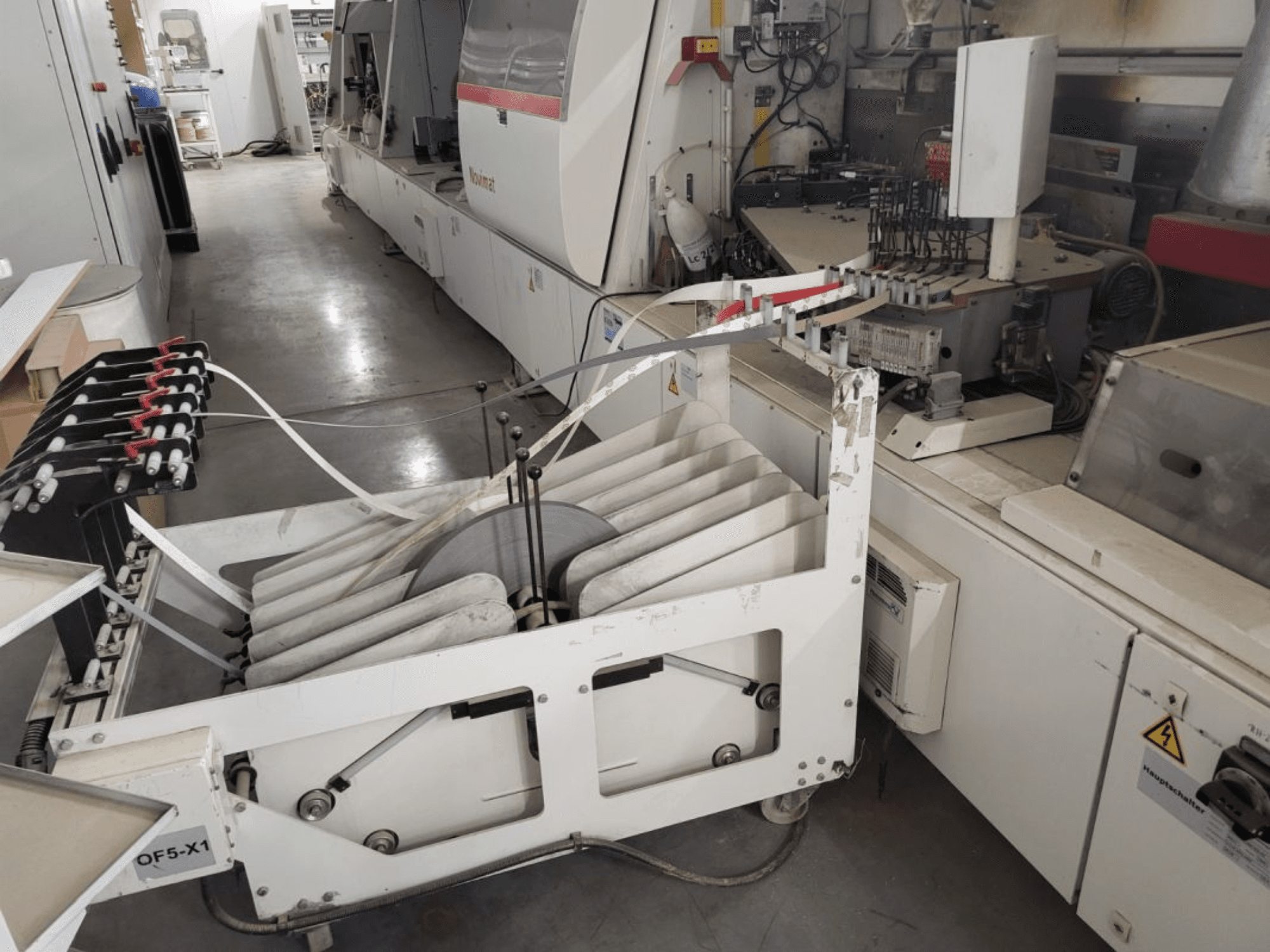 IMA Novimat/I/680/650/R3 edgebander, side view showcasing feeding rollers and control panel amidst workshop environment.