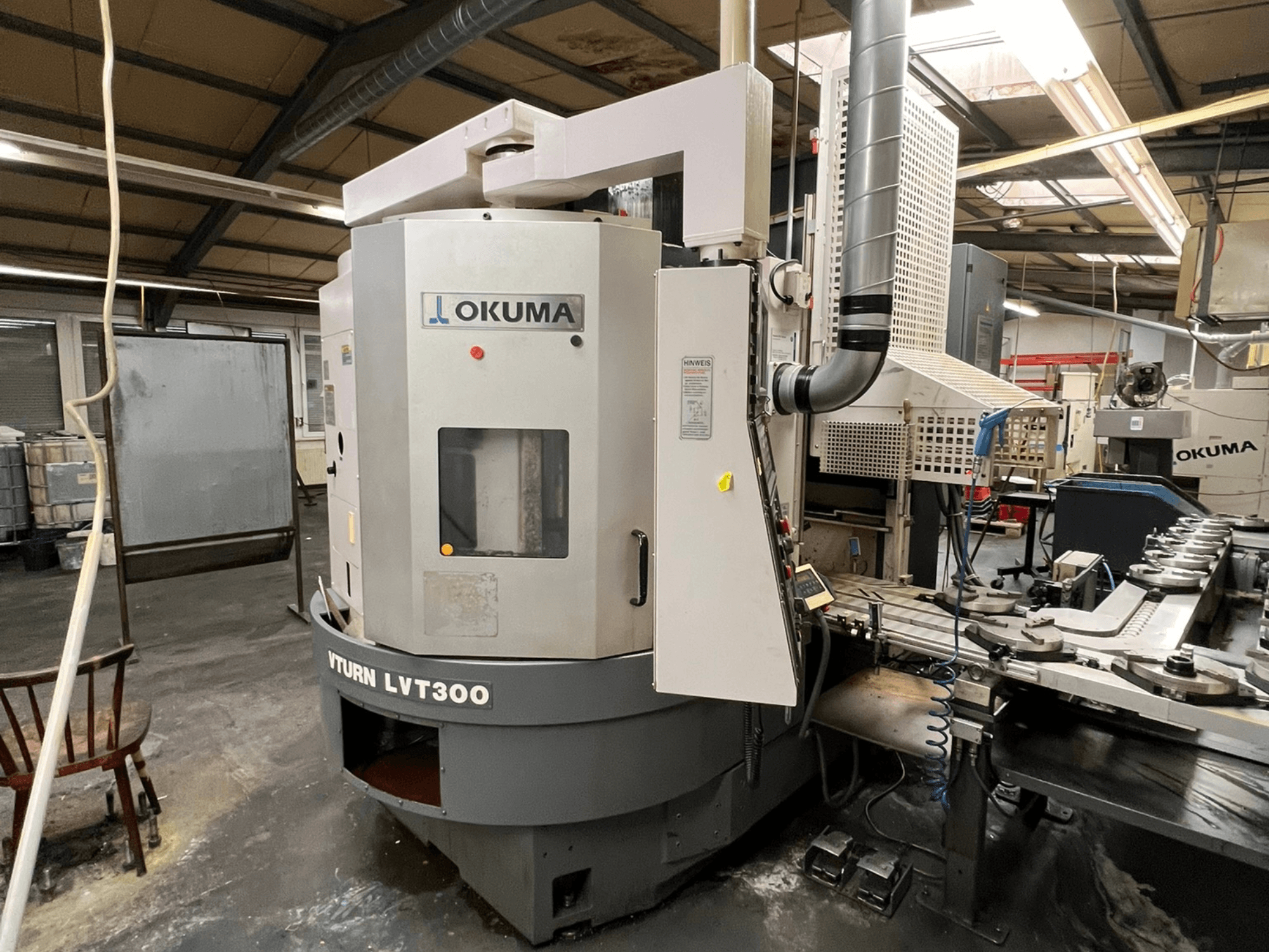 Okuma Vturn LVT300 CNC lathe, side view in industrial setting, showcasing control panel and coolant system.