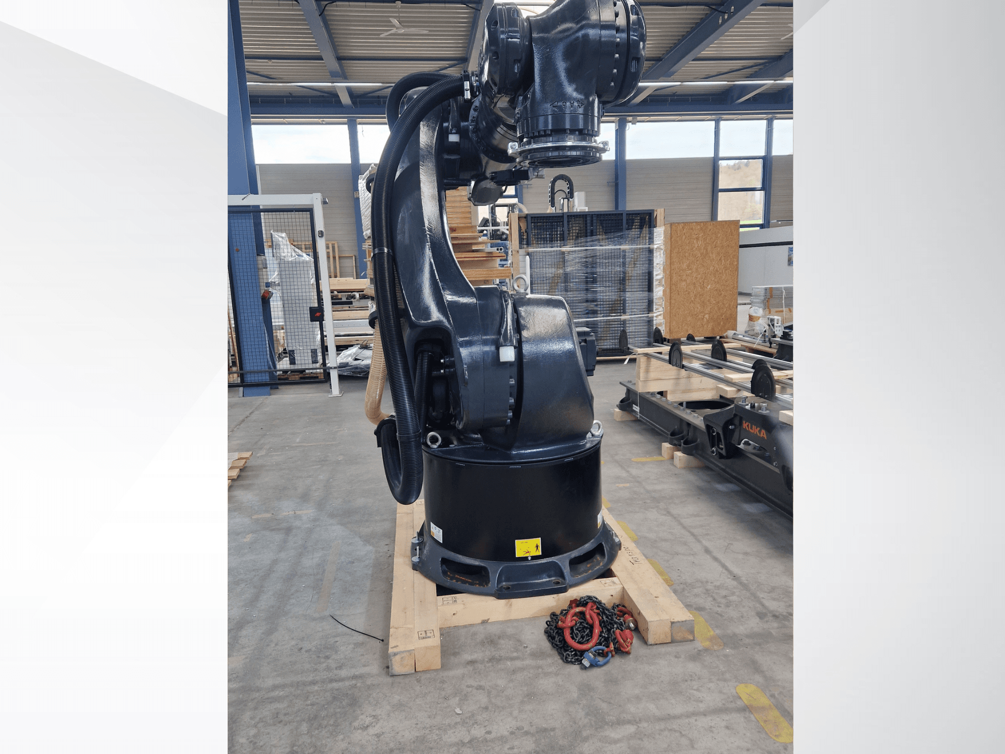 KUKA KR 340 R3330 robot arm in a warehouse, side view showcasing its base and cables, with chains in foreground.