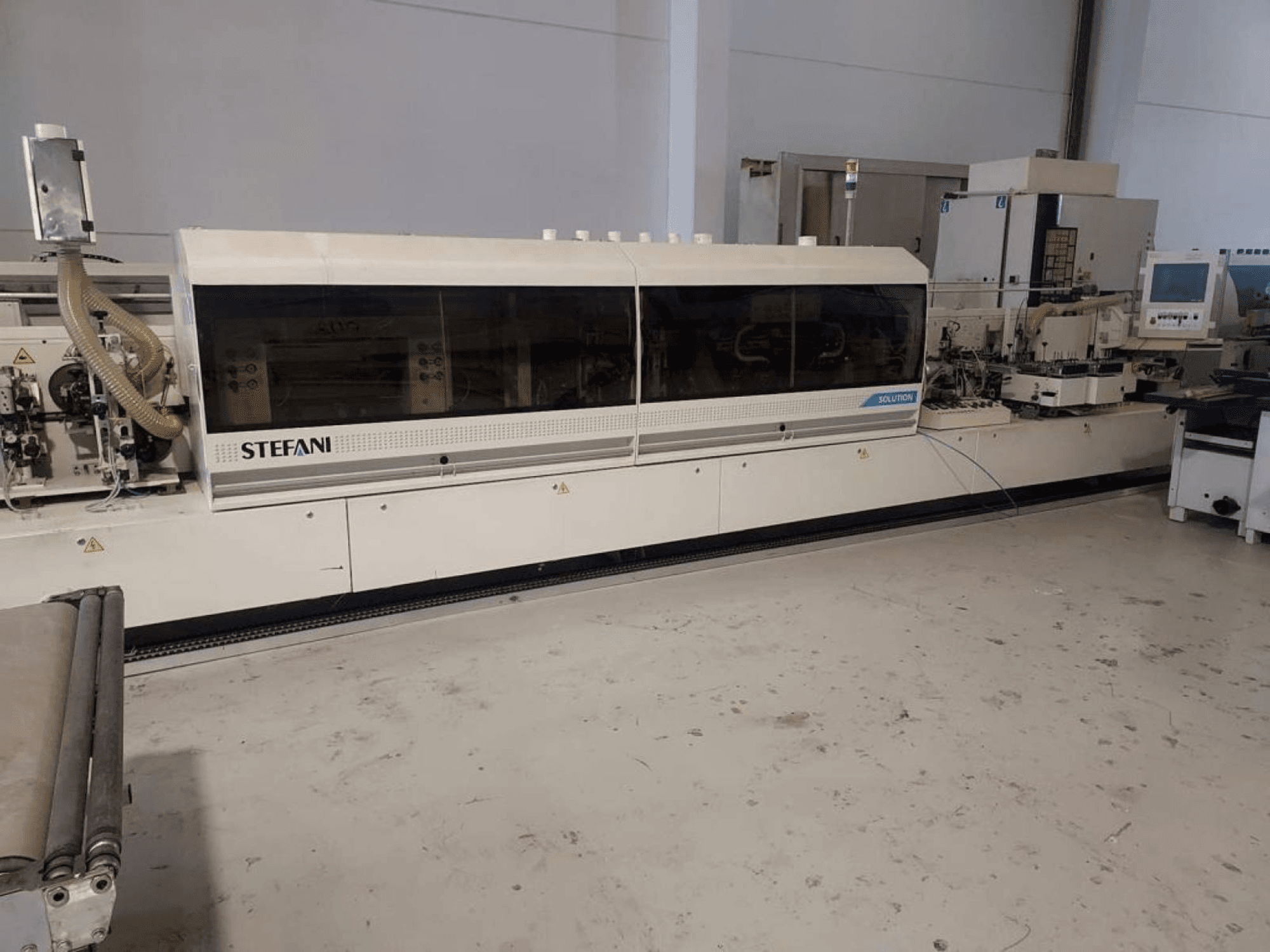 Stefani Solutions edge banding machine, front view, with dust extraction system and control panel visible, in a workshop setting.