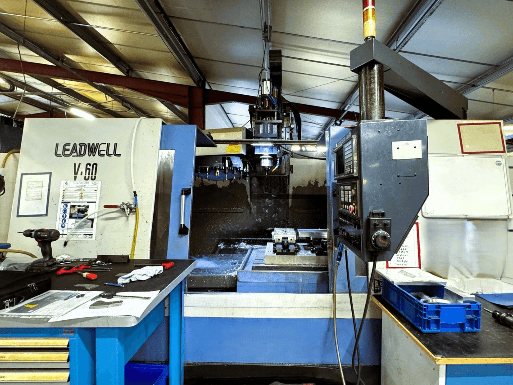 Leadwell V-60 vertical machining center from a side view, showcasing control panel and work area with tools and parts.