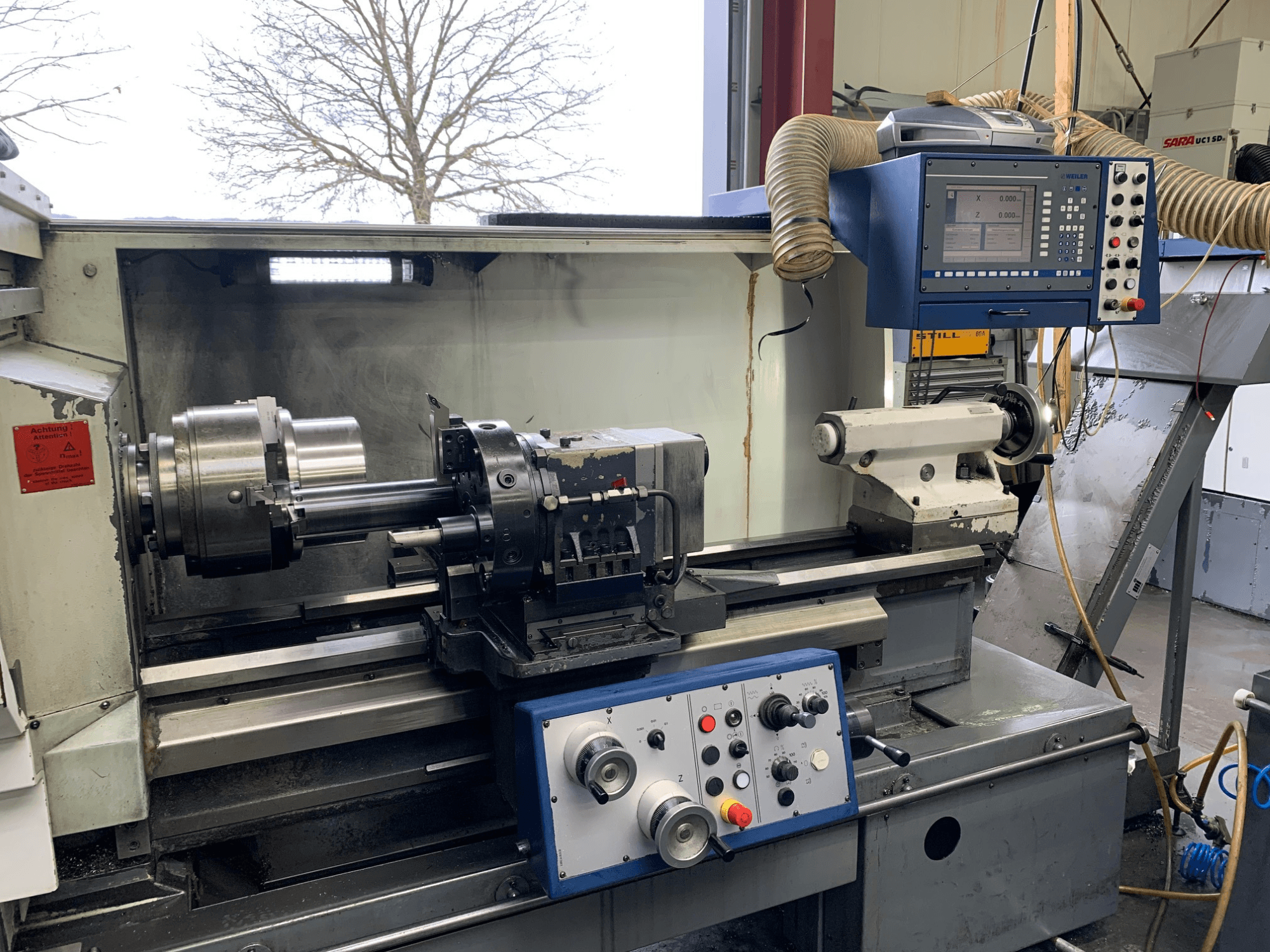 Weiler E55X1000 horizontal turning machine in a workshop, showing the control panel, lathe, and tool holder. Front view.