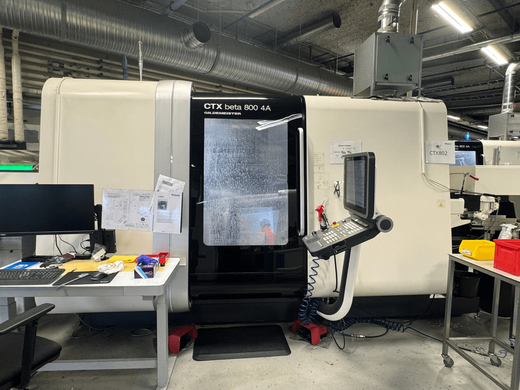 CTX beta 800 4A CNC machine in a workshop, side view showing control panel and workspace cluttered with tools and documents.