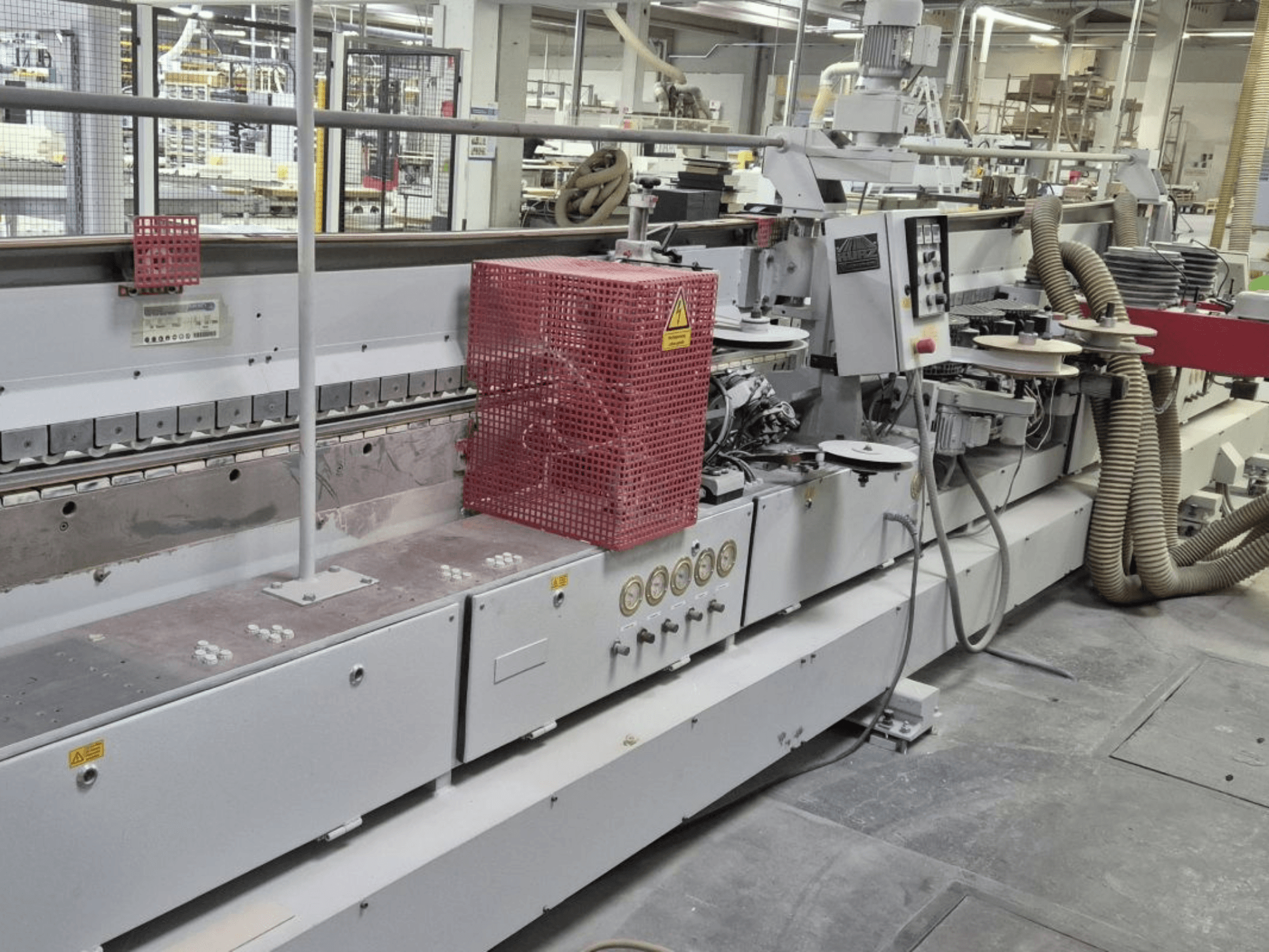 Edge banding machine with control panel, suction hoses, and a red safety cover, viewed from a side angle.