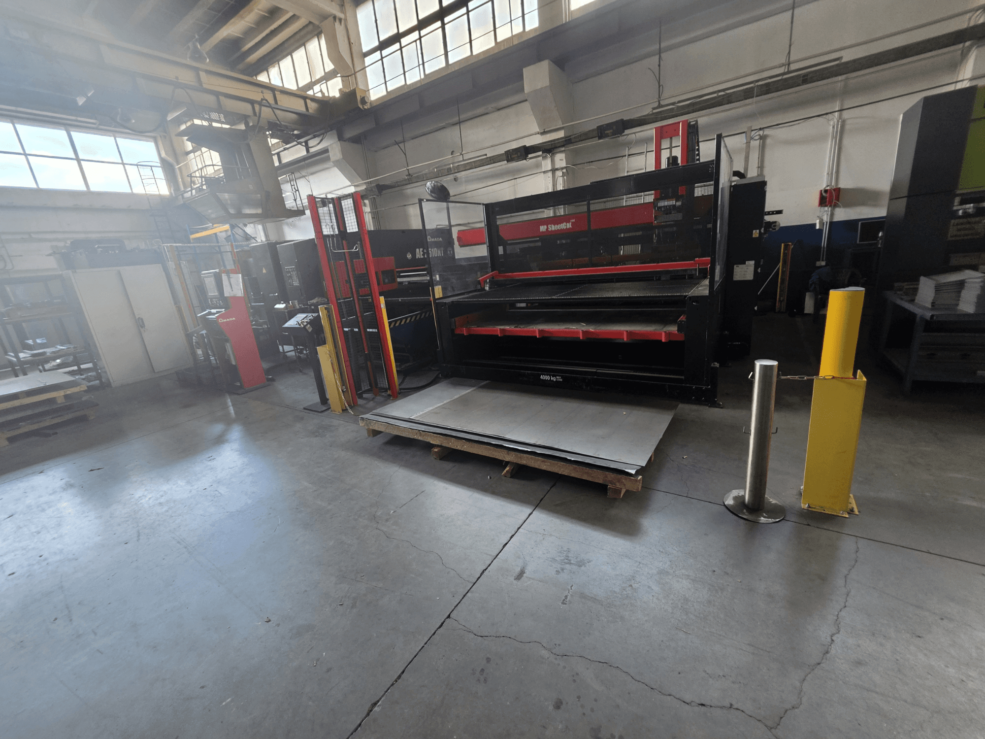 CNC Punching Machine AMADA AE-2510NT in warehouse, viewed from a side angle, showcasing machine setup and metal sheets.