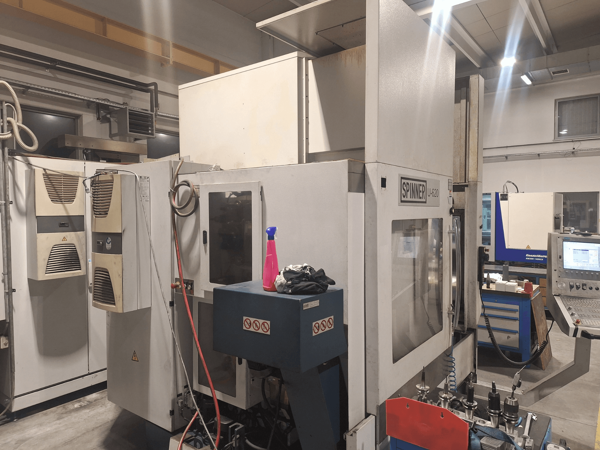Spinner U-620 CNC machine shown from a front view in a workshop, featuring control panel and various tools on a workbench nearby.