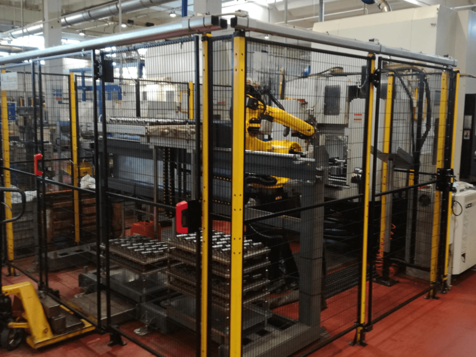 Enshu EV450 vertical machining center in a fenced workspace, featuring robotic arms and multiple stacked workpieces. Front view.