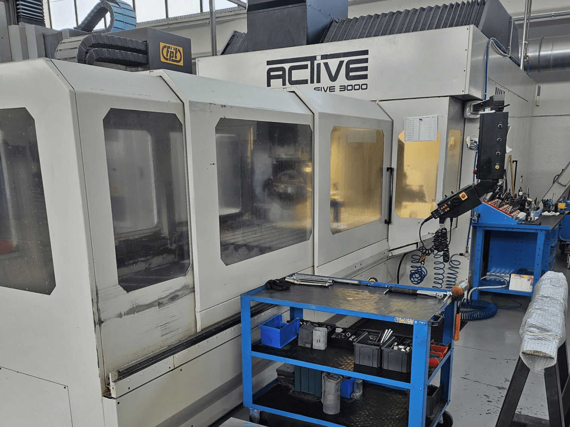 Active 3000 CNC machine in a workshop, front view with tools on a blue cart, visible controls and work area inside.