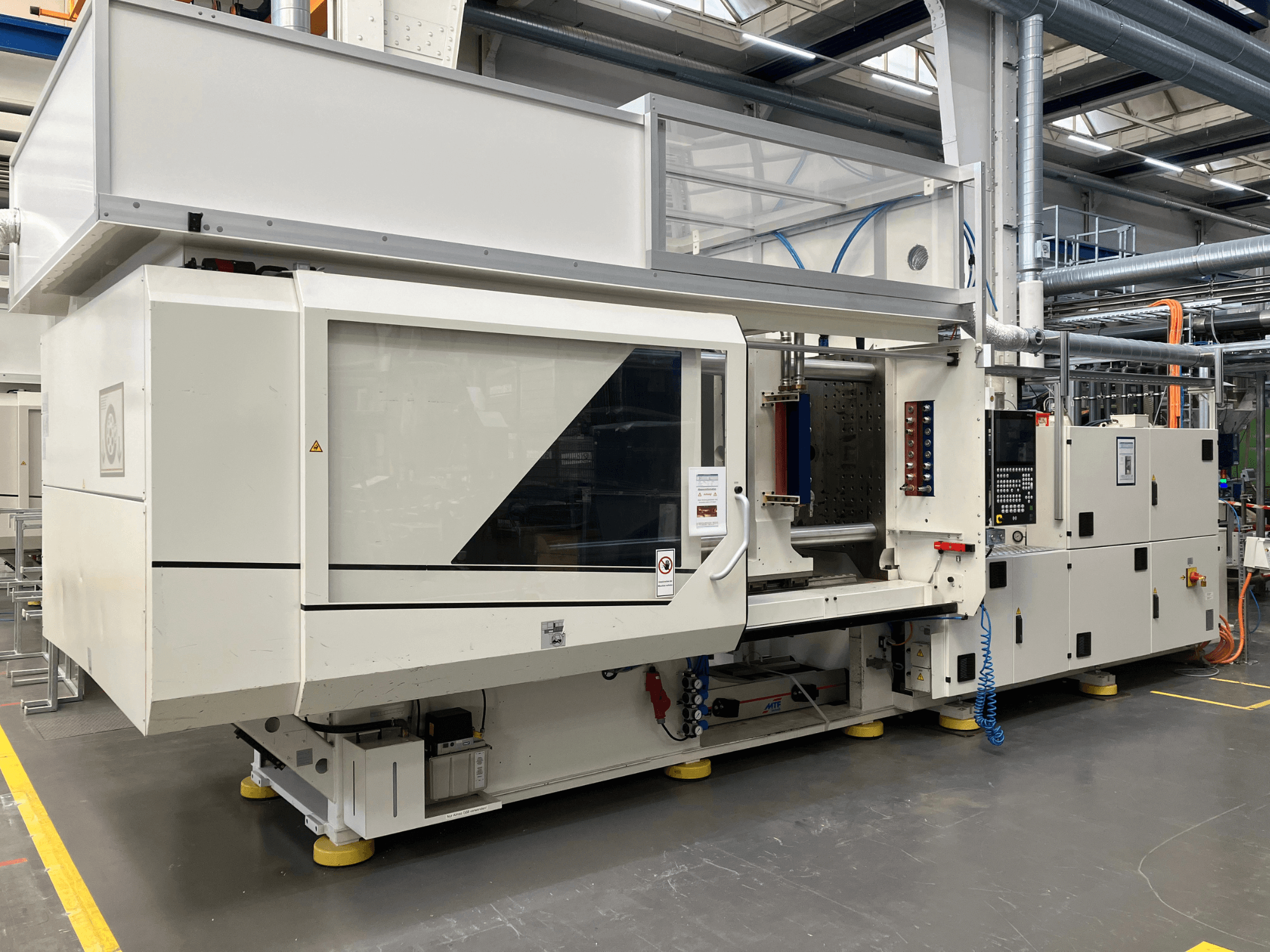 Side view of an injection molding machine, model AET, featuring control panel and transparent covers, in an industrial setting.