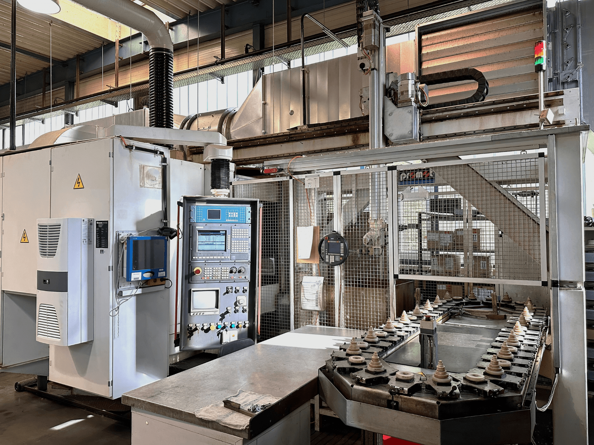 Industrial machinery with control panel, cooling unit, and conveyor. Front view, featuring bright lights and safety signage.