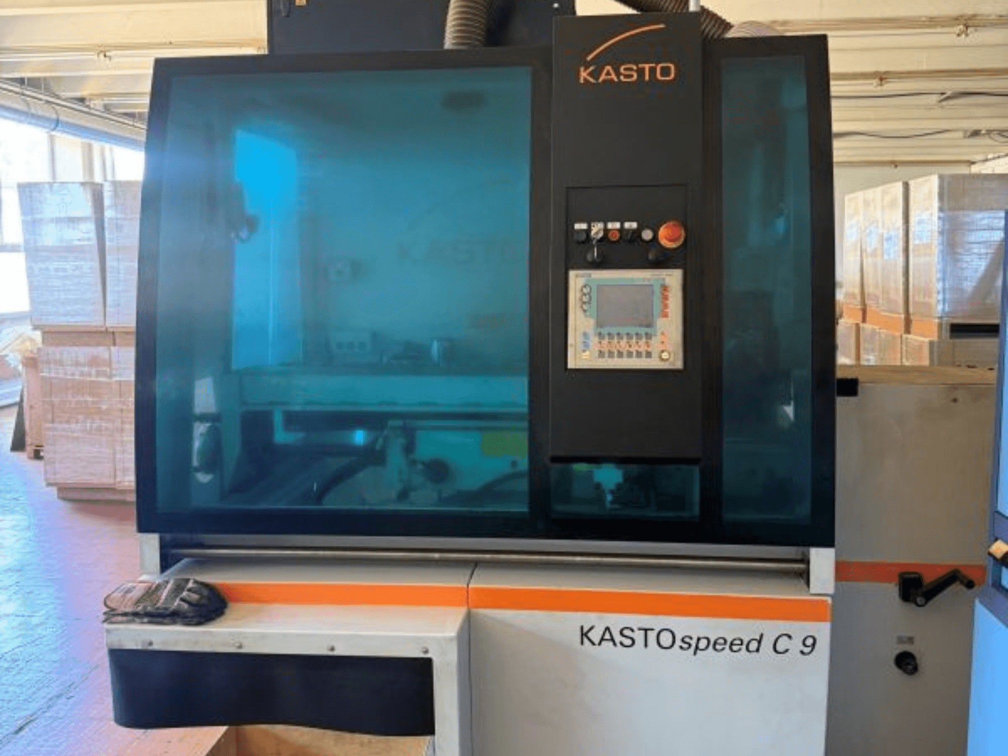 Front view of KASTO KASTOspeed C 9 circular metal saw, featuring control panel and safety glass, with wooden crates in background.
