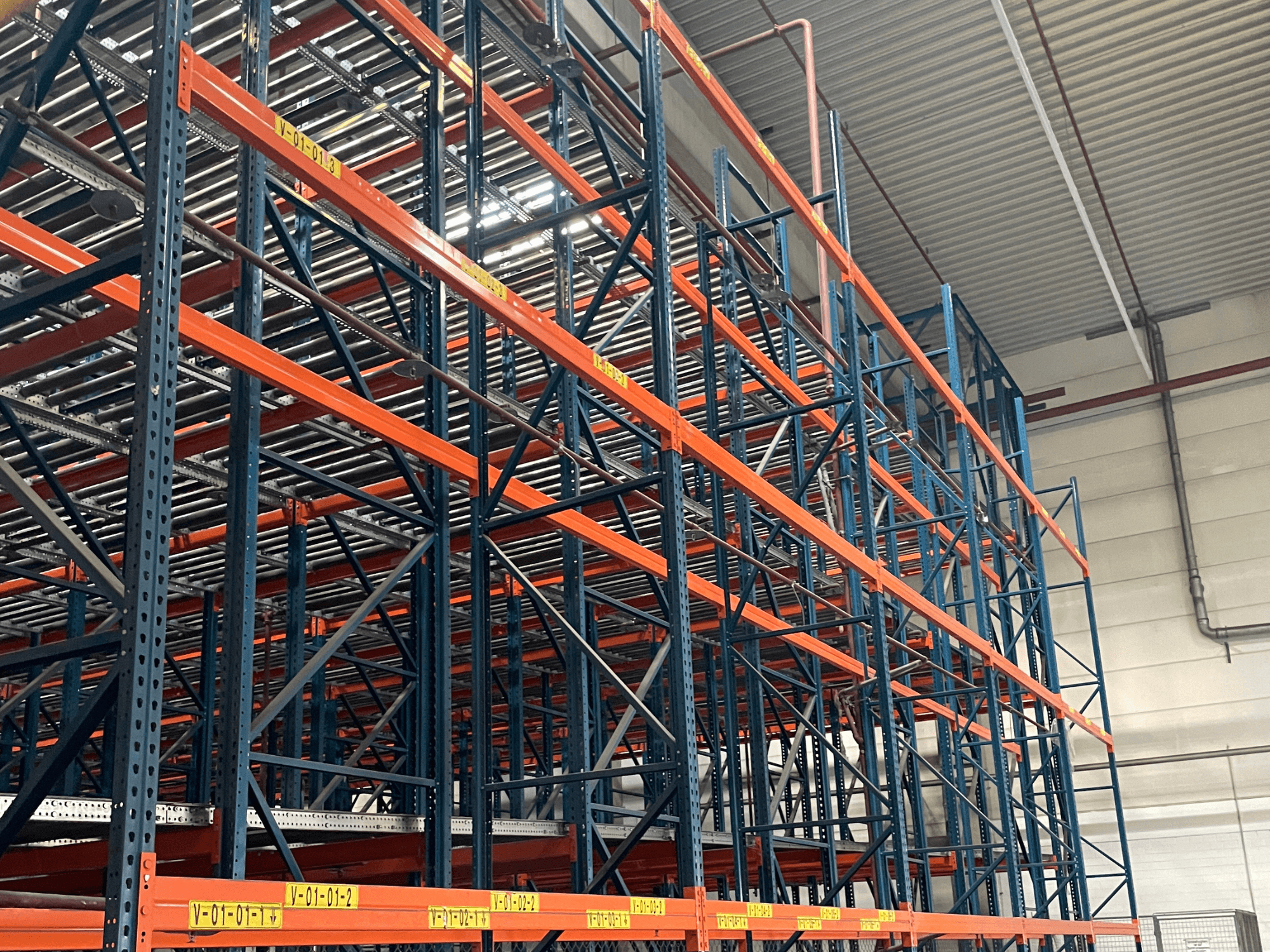FL SYSTEME F05.10 FLG pallet handling system in a warehouse, shown from a side view, featuring heavy-duty orange and blue racking.