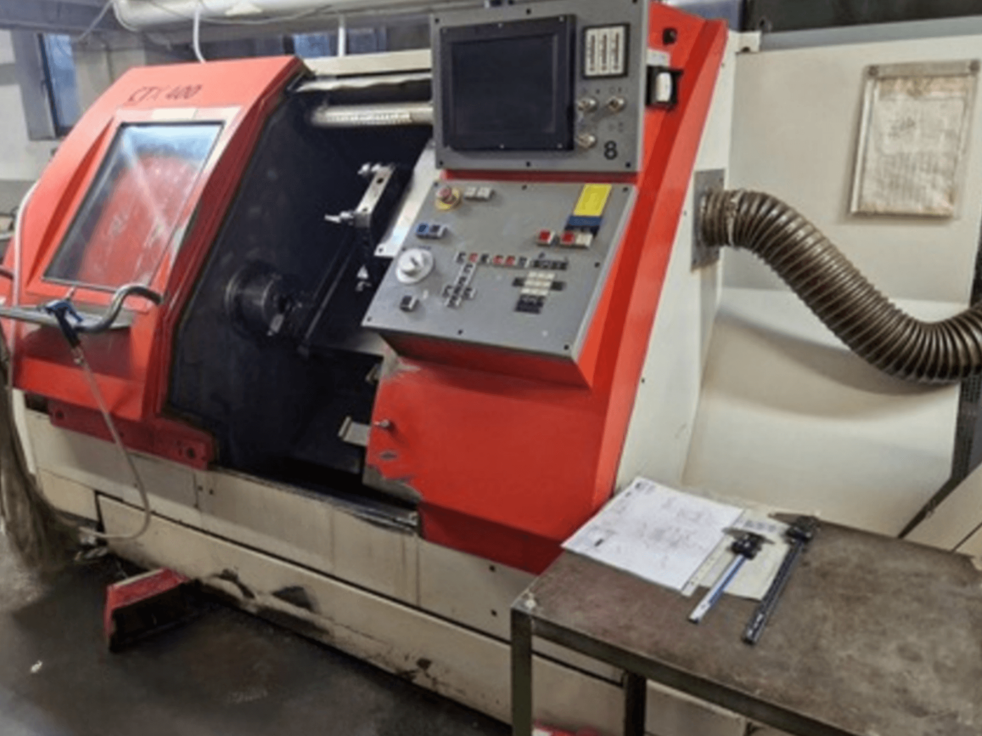 Gildemeister CTX 400 horizontal turning machine, front view with control panel and exhaust hose. Includes measuring tools on table.