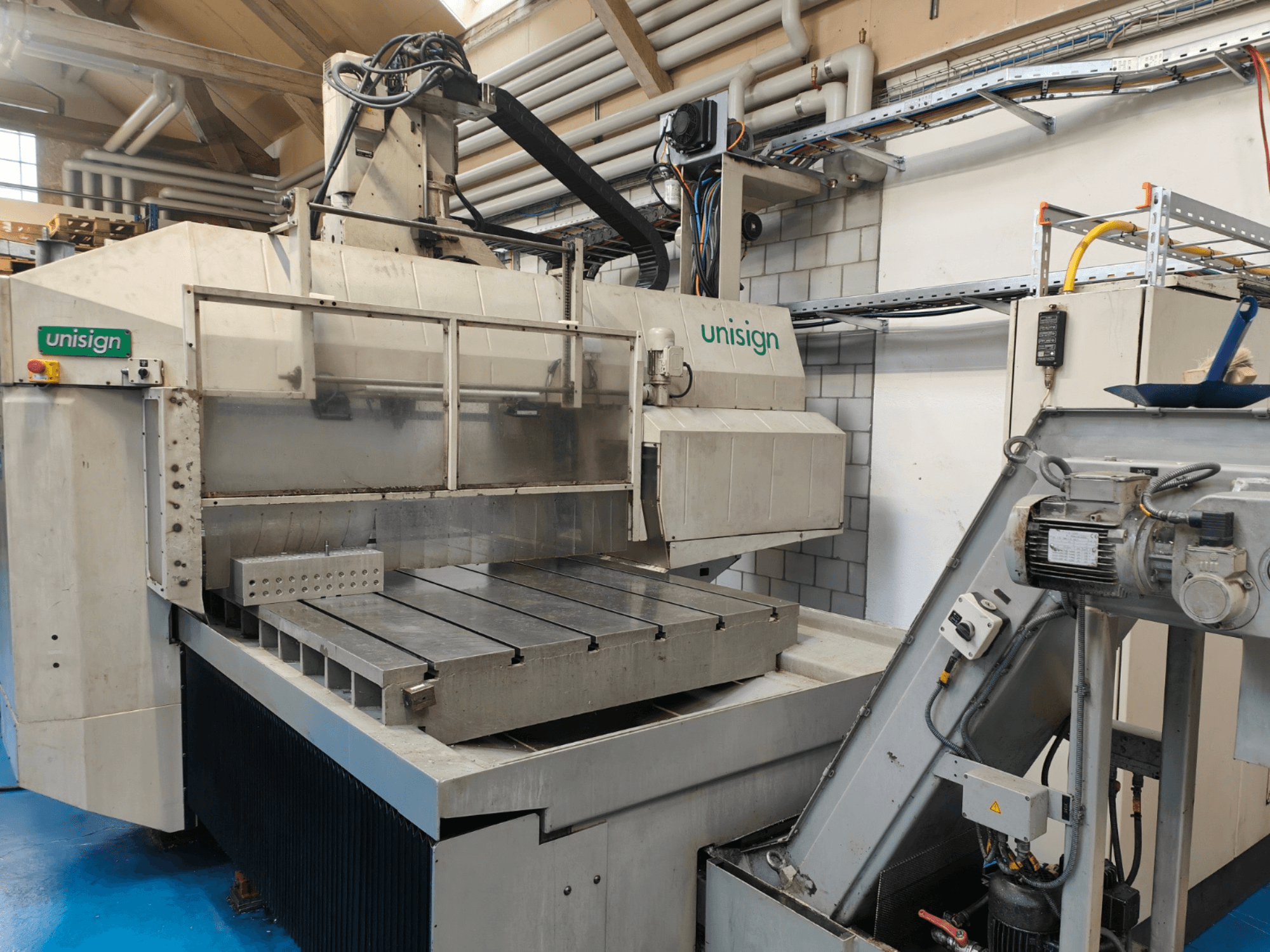 Unisign CNC machine in a workshop, front view, featuring a large table, control panel, and industrial design elements.
