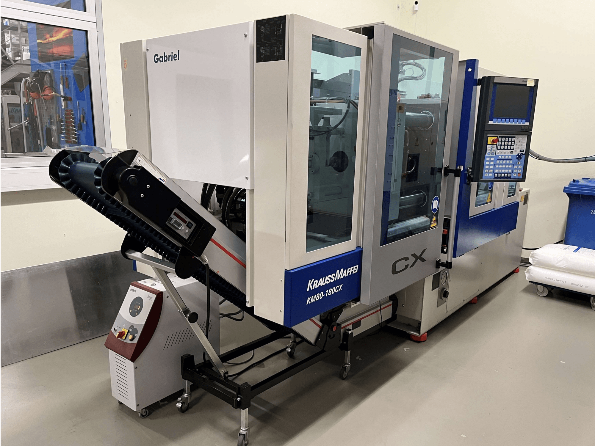 Hydraulic injection moulding machine Krauss Maffei KM 80-180 CX, front view, with control panel and conveyor system.