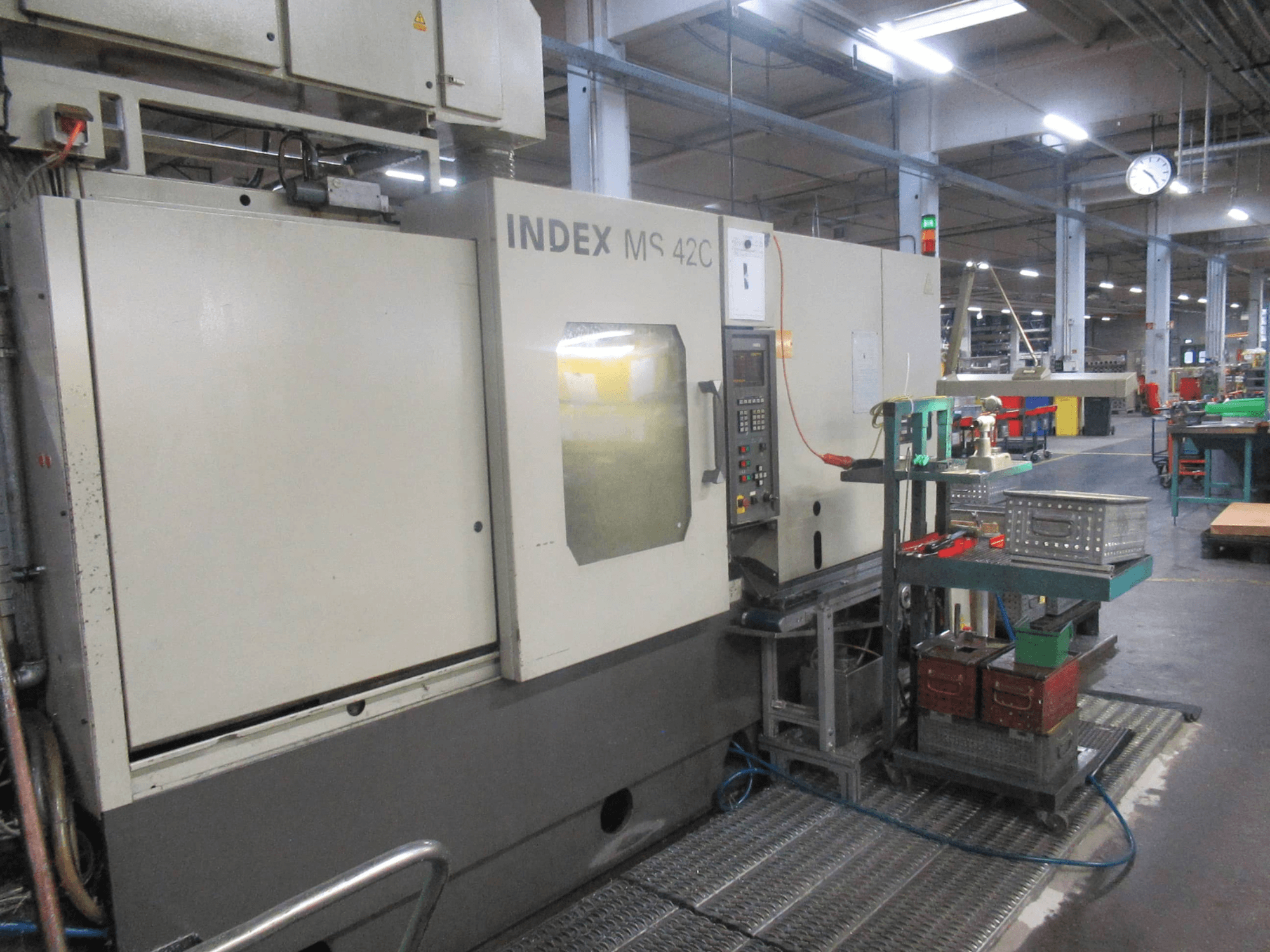 INDEX MS 42C CNC machine in a workshop, side view showing control panel and tool storage on wheeled cart.