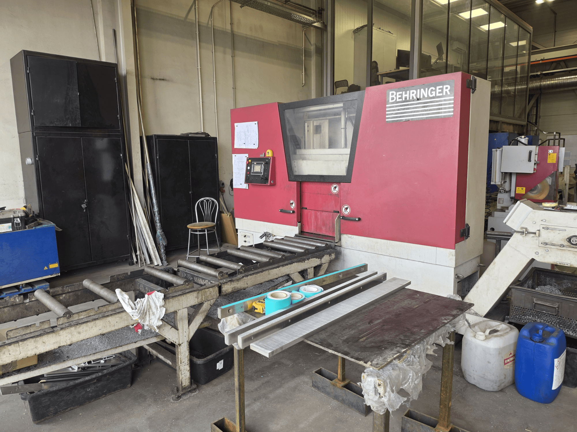 Behringer HBE 511 A metal band saw in a workshop setting, front view with rollers and work surface nearby.