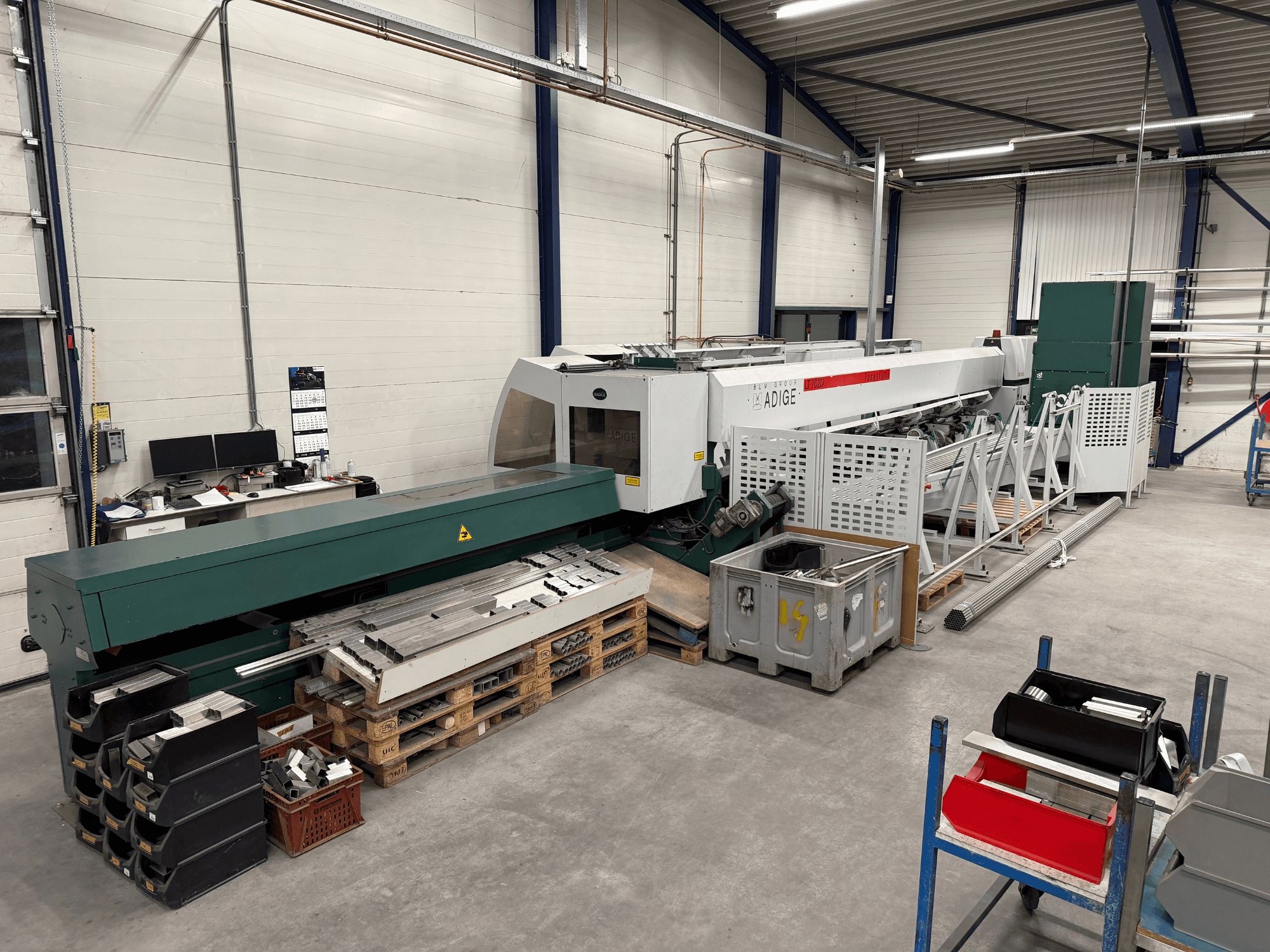 BLM Adige LT702 CO2 laser cutting machine in a workshop, side view with metal components and workspace clutter visible.