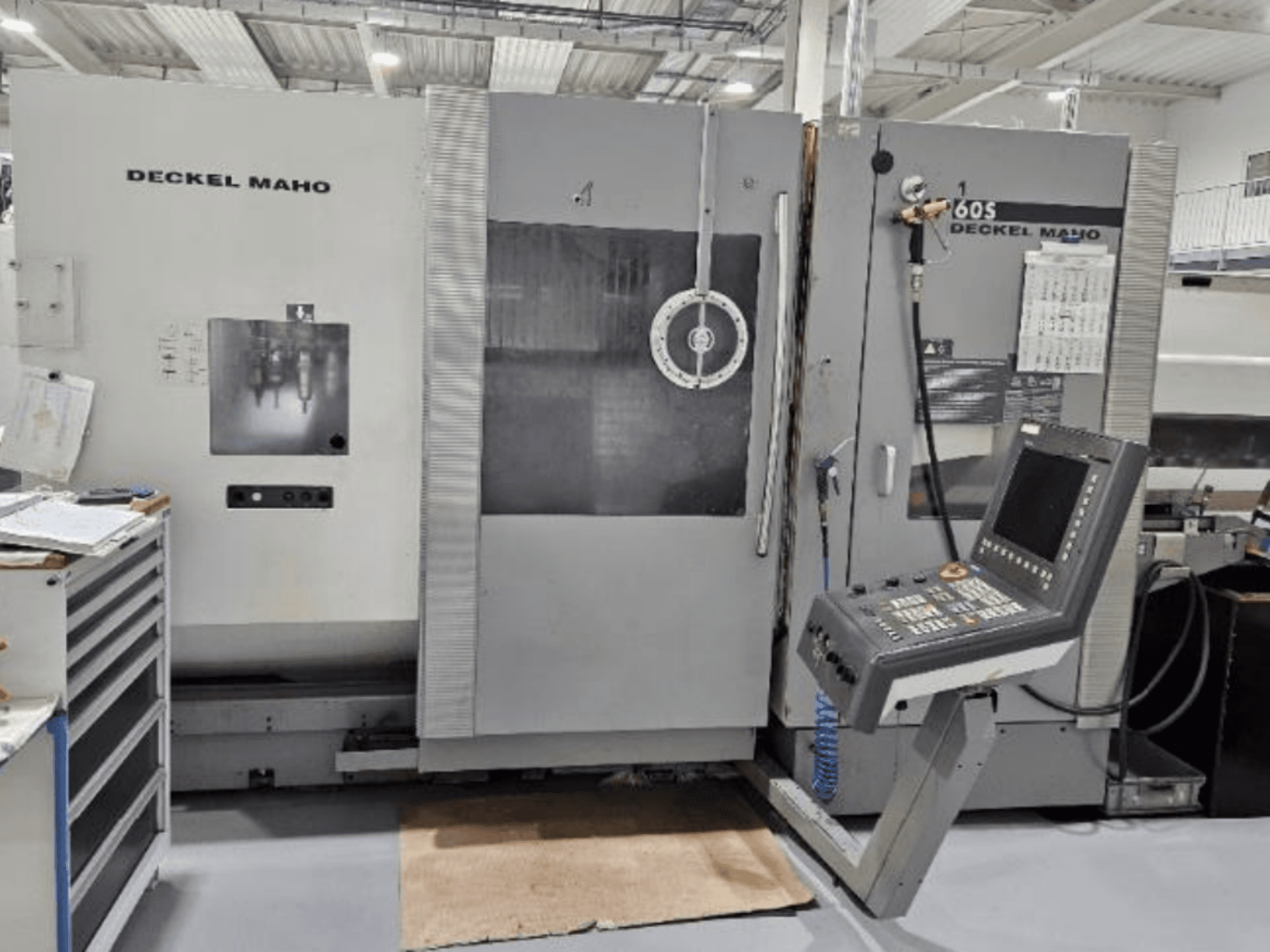 Front view of a DECKEL MAHO 60S CNC machine with control panel, tools visible, in a workshop setting.