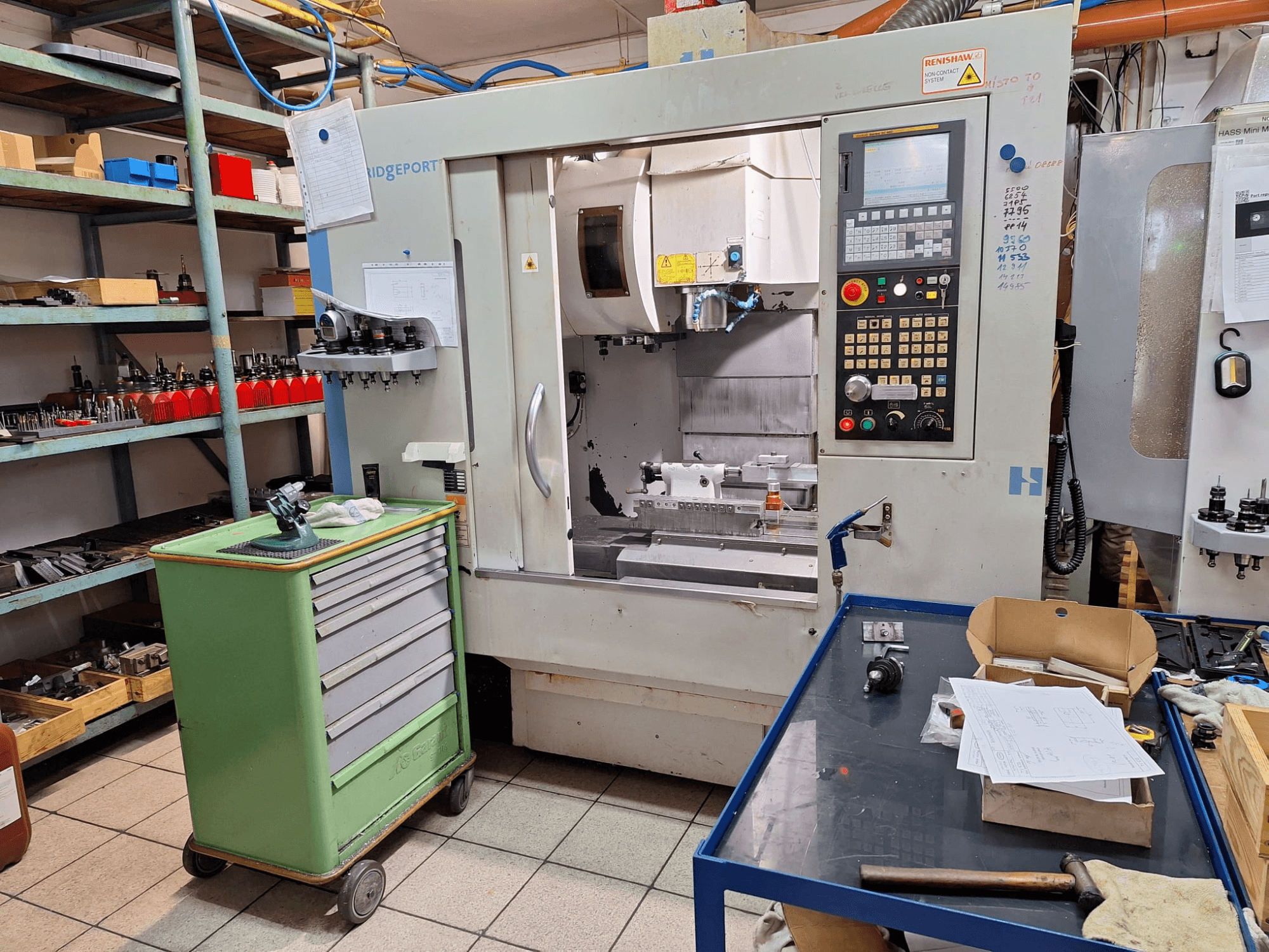 Front view of Hardinge Bridgeport GX 710 vertical machining center with control panel, tools, and shelves in a workshop setting.