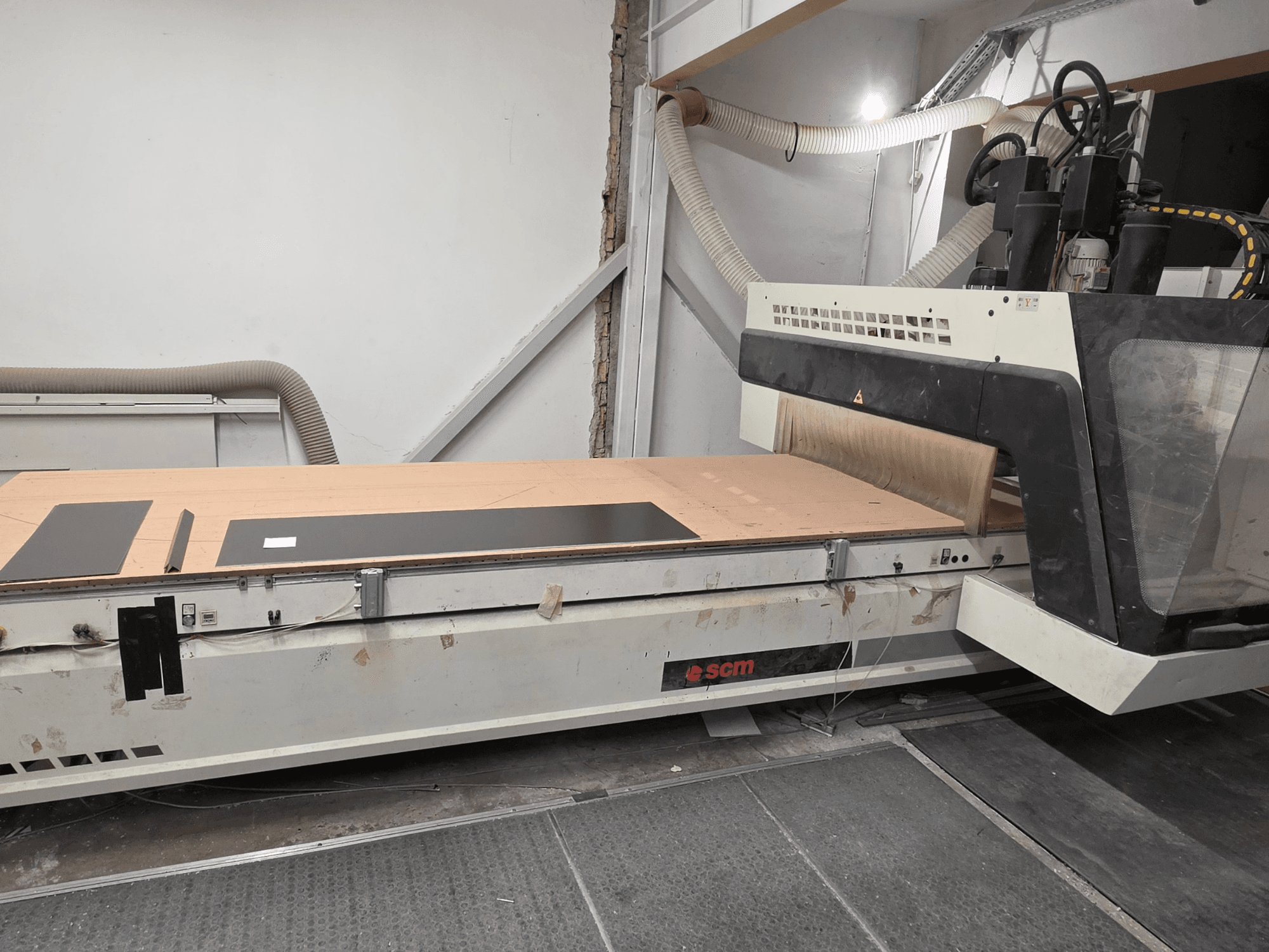 SCM RECORD 132 CNC wood machining centre in side view, featuring a flat working table with black workpieces and dust collection system.