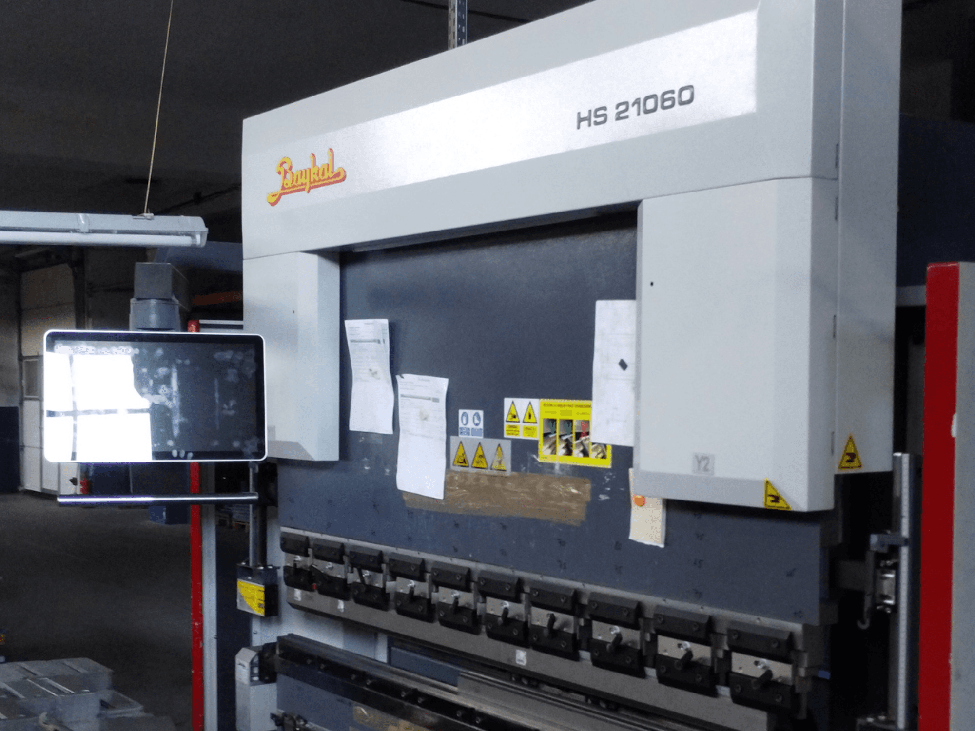 Baykal APHS 21060 press brake front view, featuring control display, safety warnings, and metal bending tools.