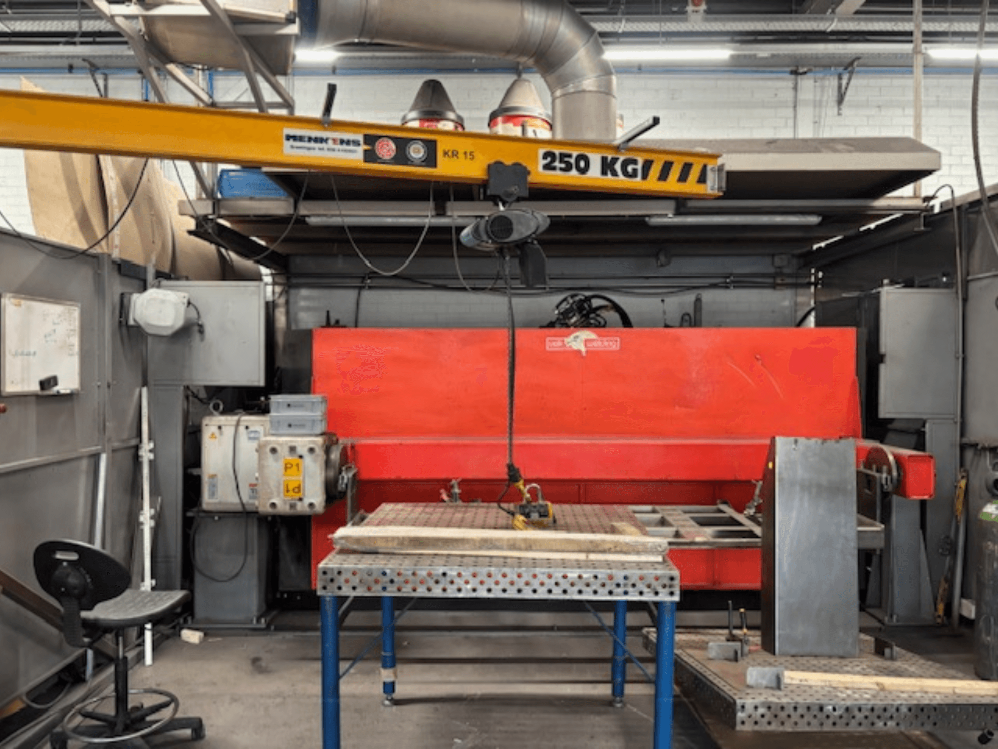 Industrial workshop with a red hydraulic press, overhead crane labeled "KR 15," and a metal worktable, side view perspective.