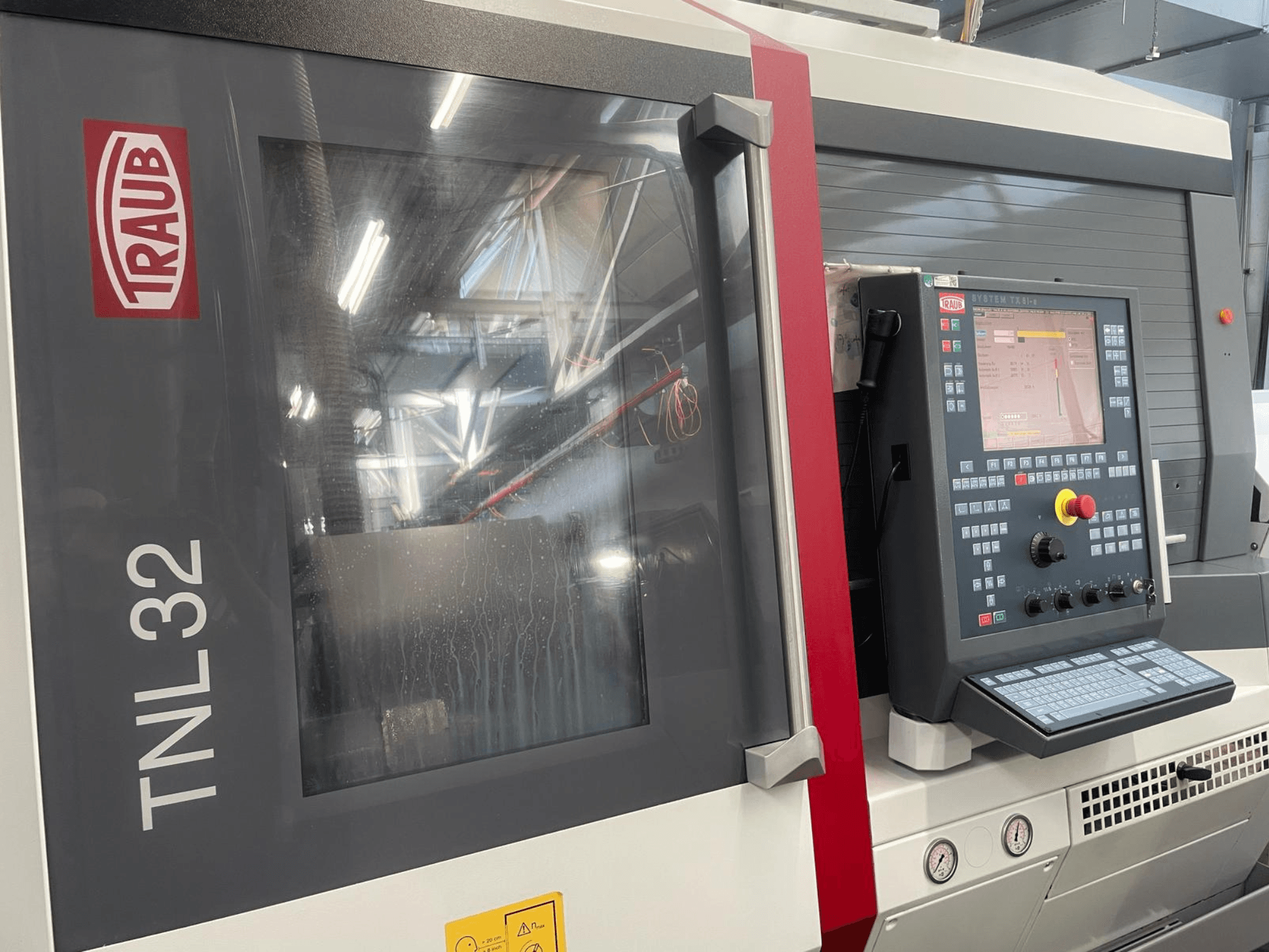 Traub TNL32 CNC lathe front view, featuring control panel with buttons, display screen, and sleek metal casing.