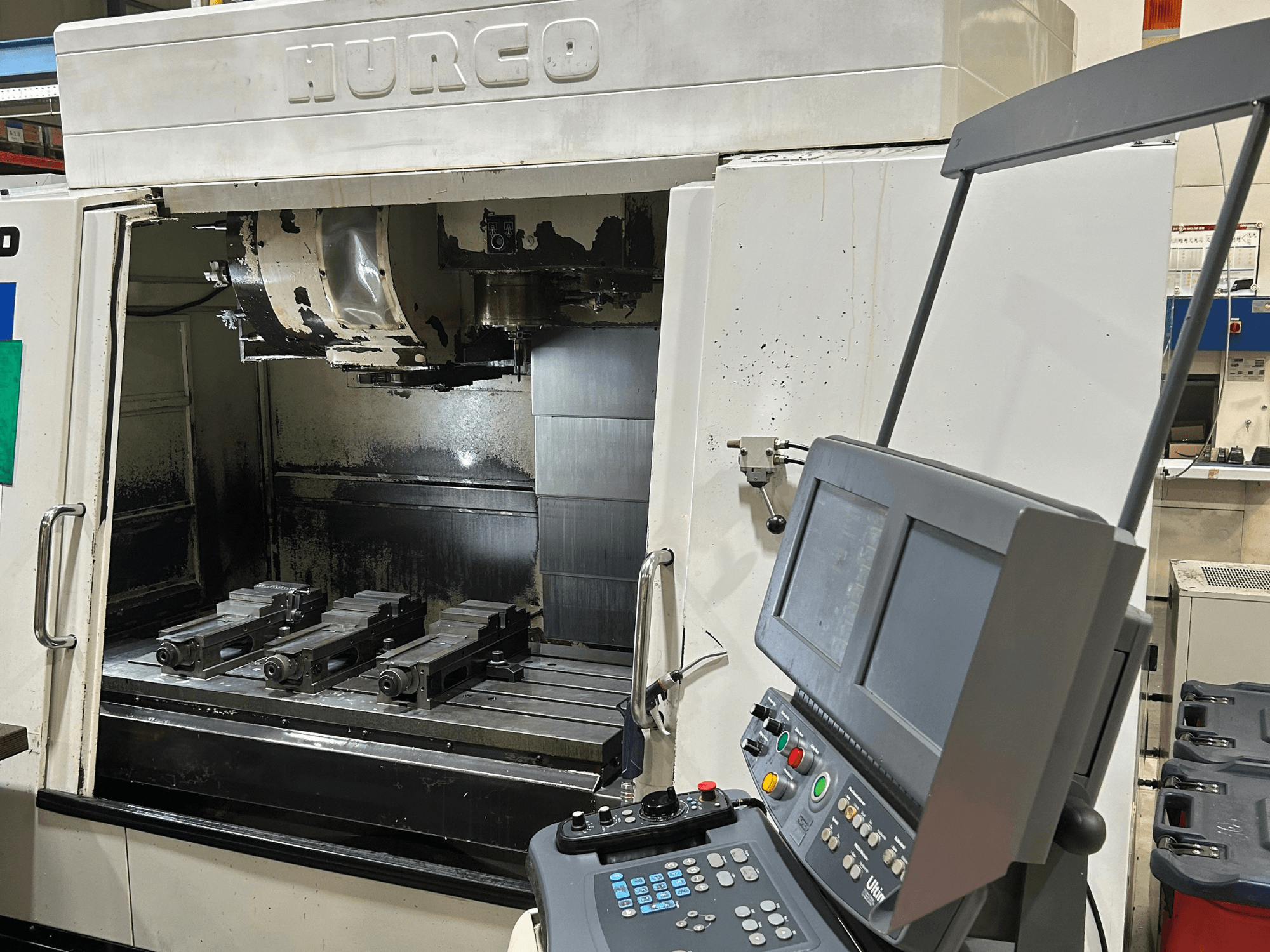 Hurco CNC milling machine, front view, with four tool holders on the table and a control panel featuring dual screens and buttons.