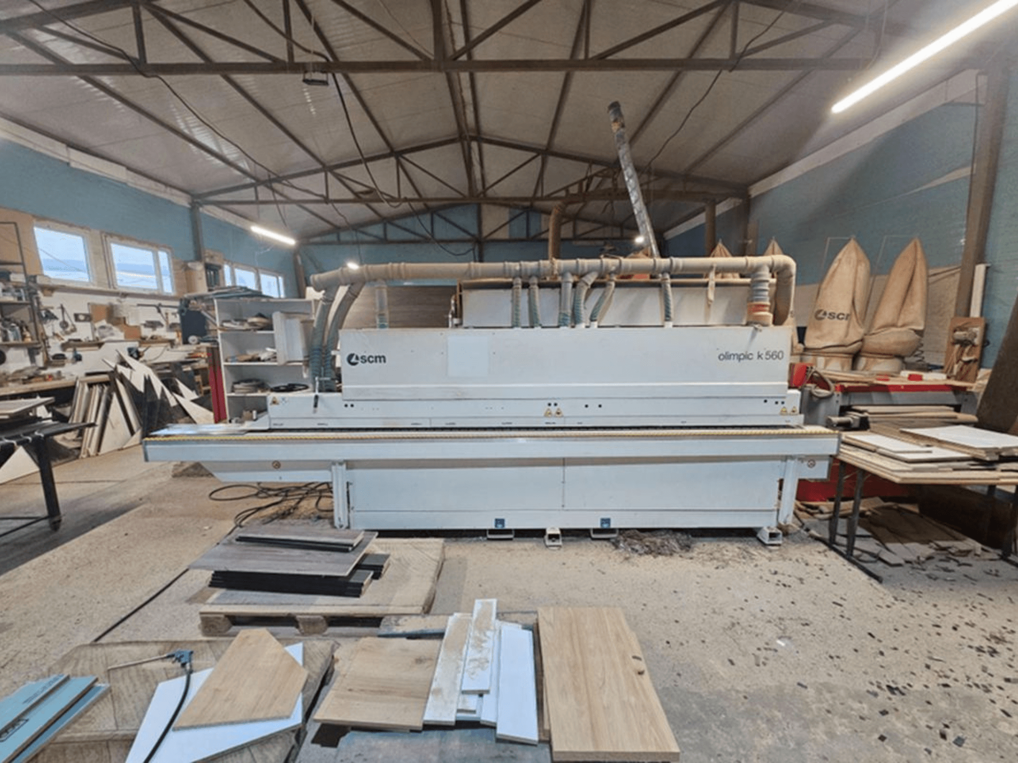 SCM Olimpic K 560 edgebander shown in a workshop, front view; features visible include feed rollers and exhaust system.