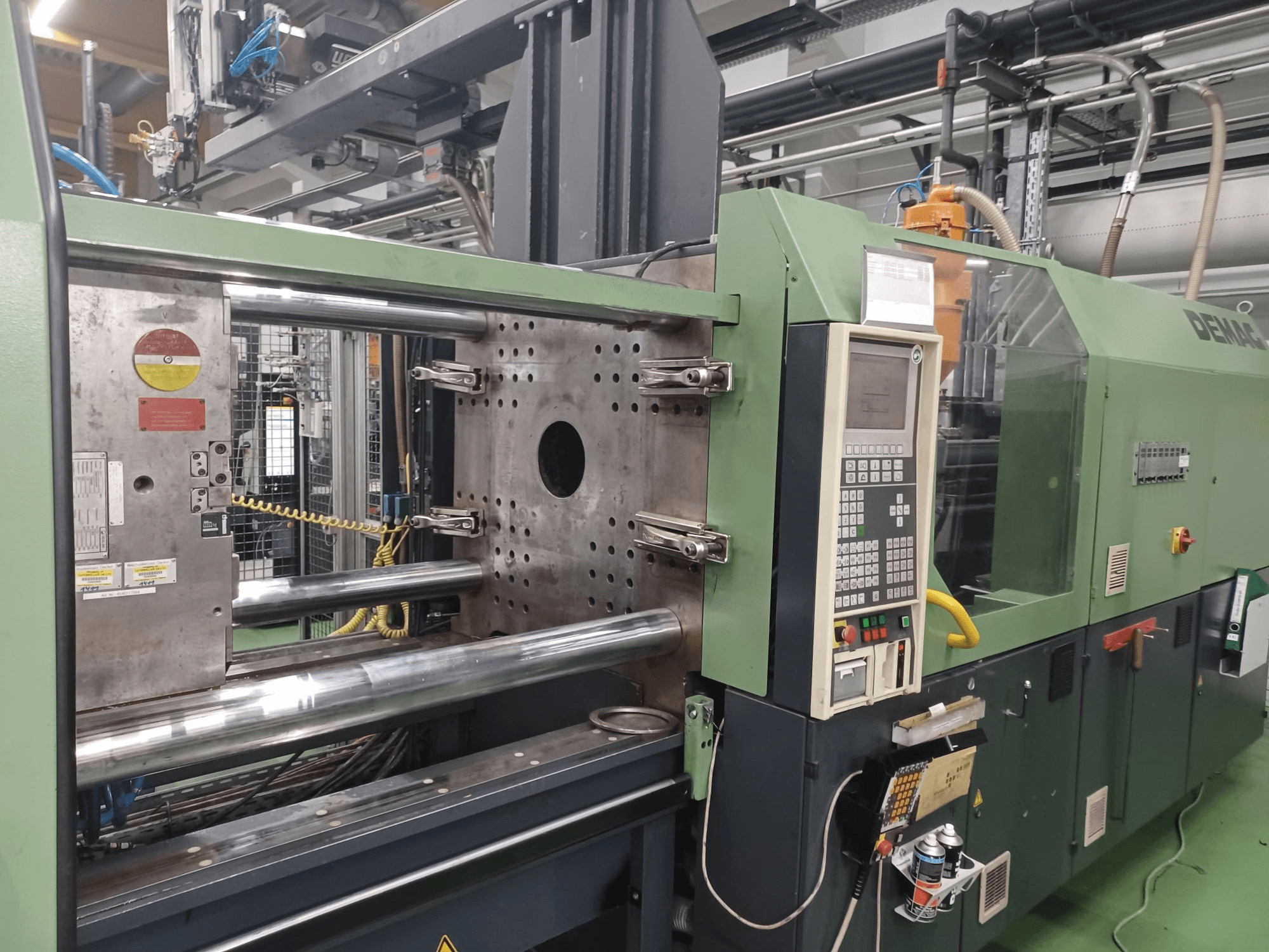 Demag injection molding machine, front view, featuring control panel, metallic hydraulic cylinders, and safety features.