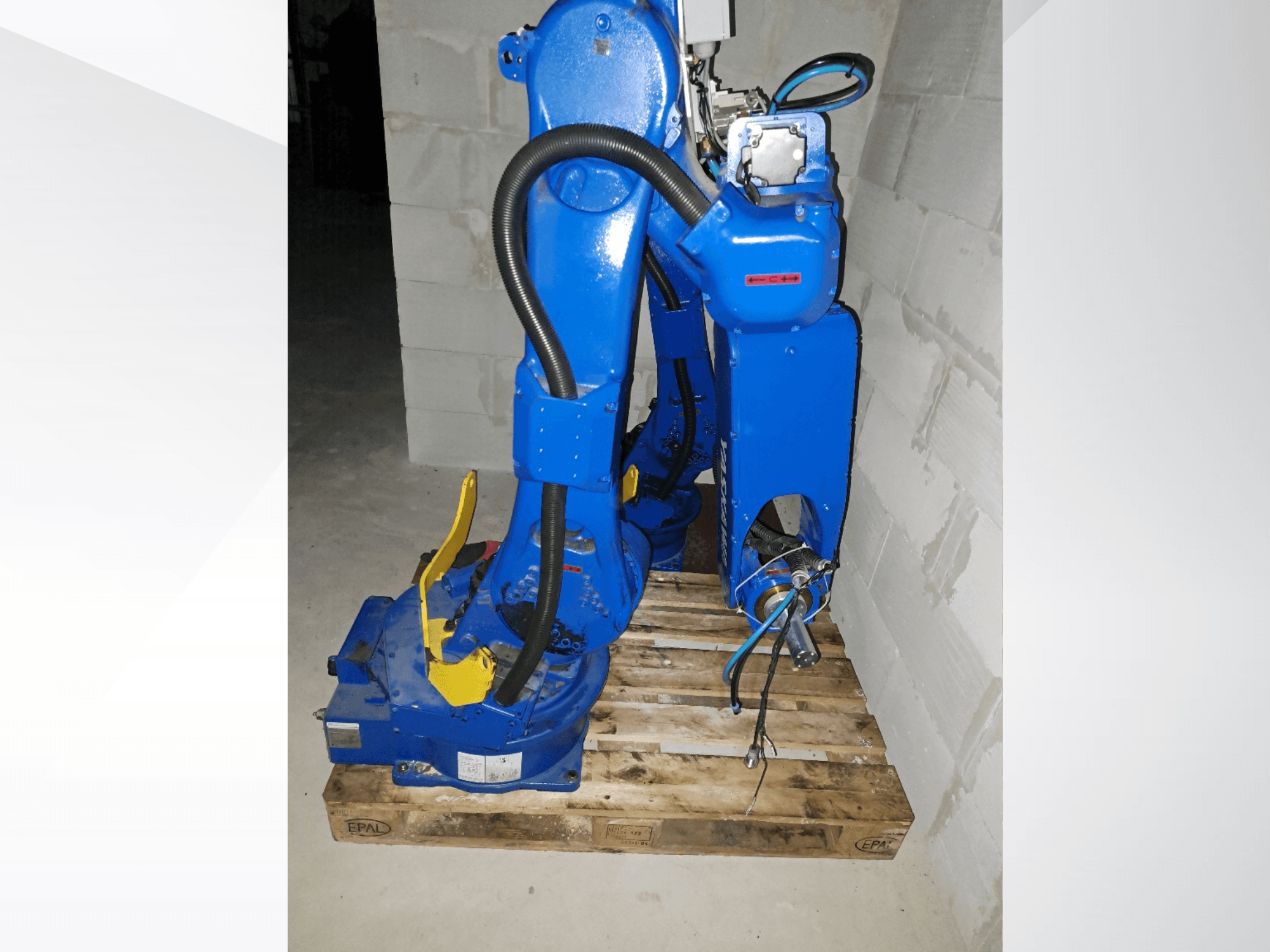 Yaskawa Motoman GP25 robot arm in blue, side view on a wooden pallet, featuring cables and mechanical joints.