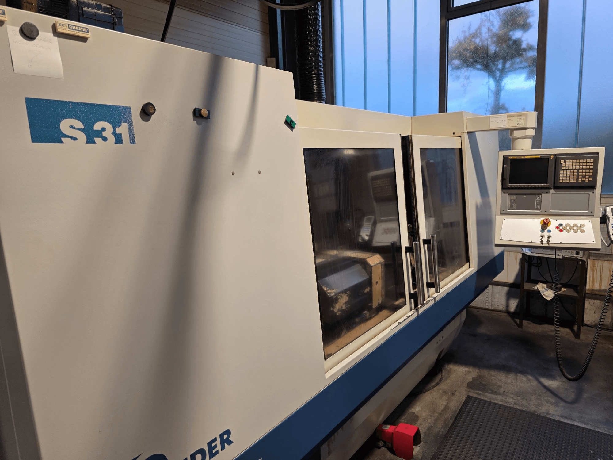 S31 CNC grinding machine, front view, features control panel with screen and buttons, large glass door, industrial environment.