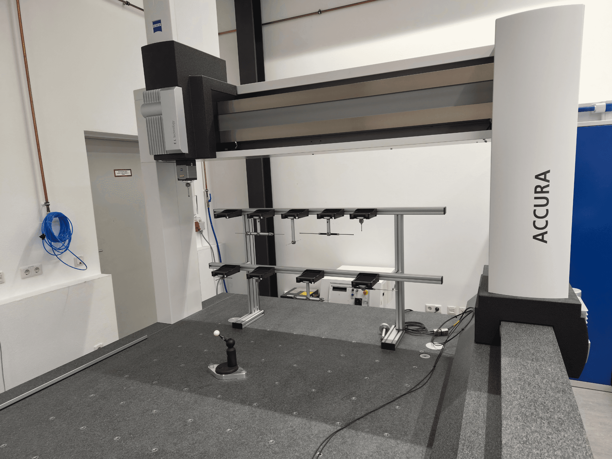 ZEISS ACCURA 16/24/10 CMM in a front view, showcasing the measuring arm, base, and control interface on a gray carpeted surface.